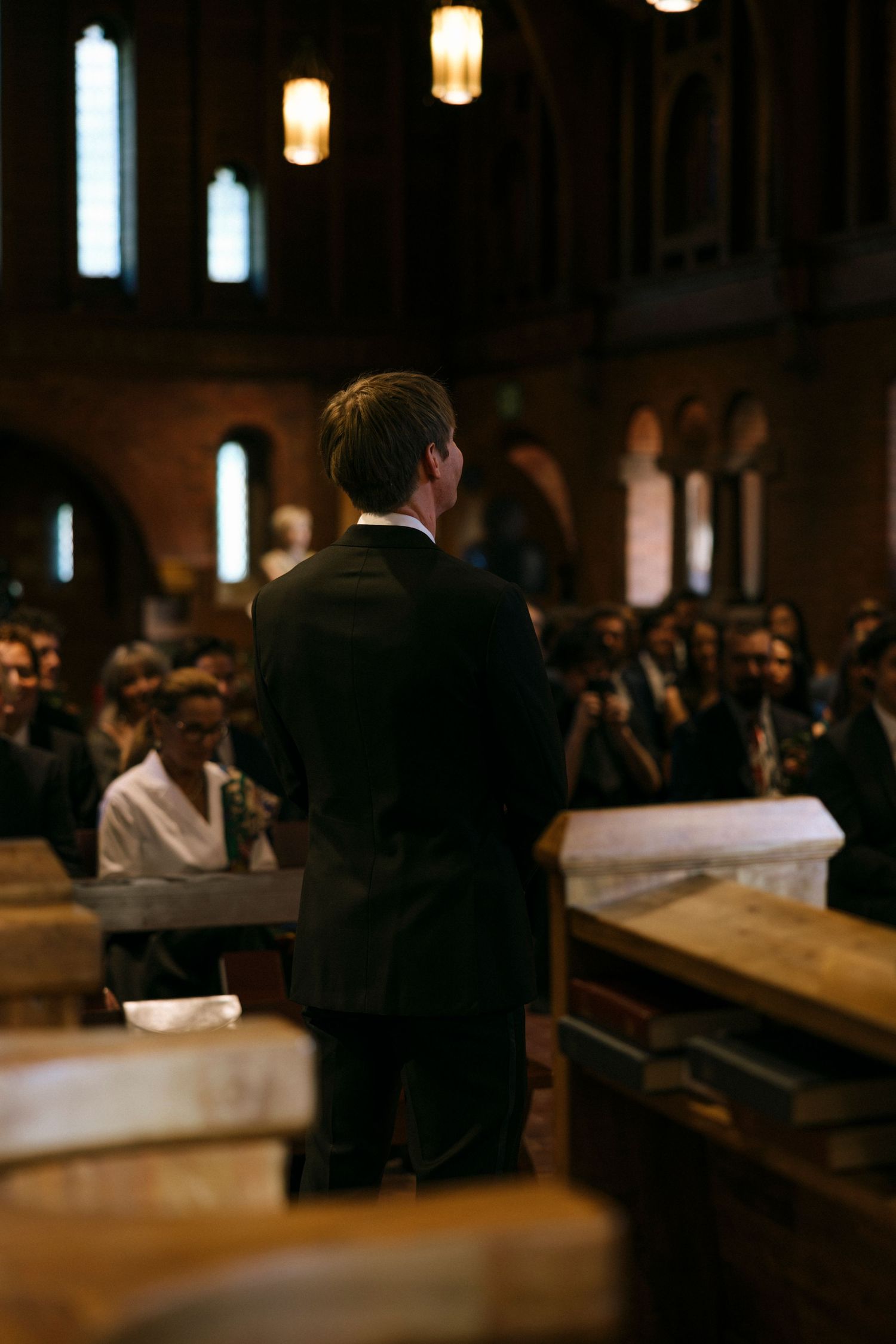 Dimly lit church interior during ceremony with guests seated in wooden pews.