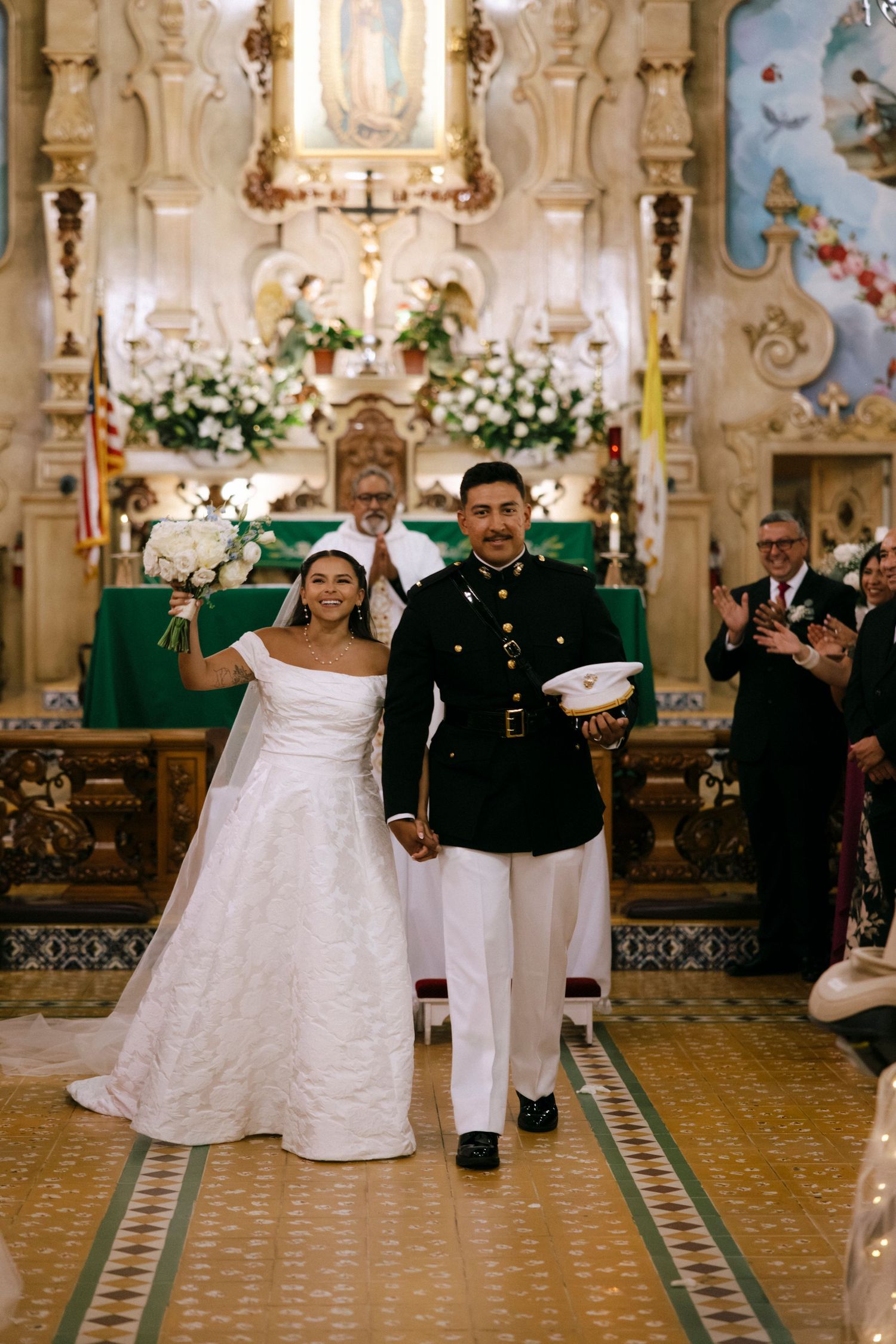 A newlywed couple walks down the aisle of an elaborately decorated church after their ceremony.