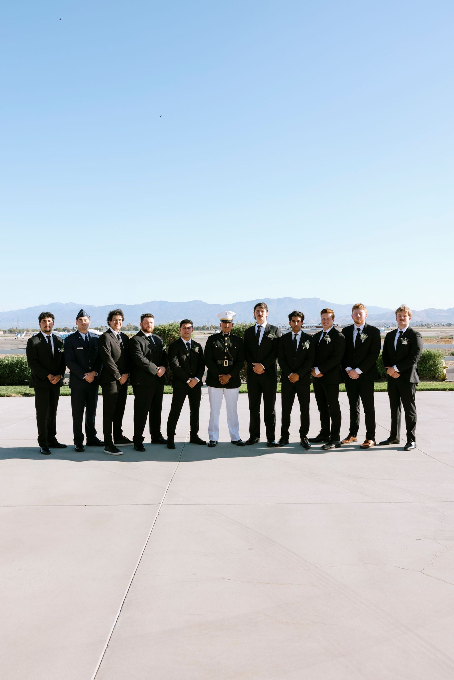 Wedding party in formal black attire forms line against desert mountain landscape.