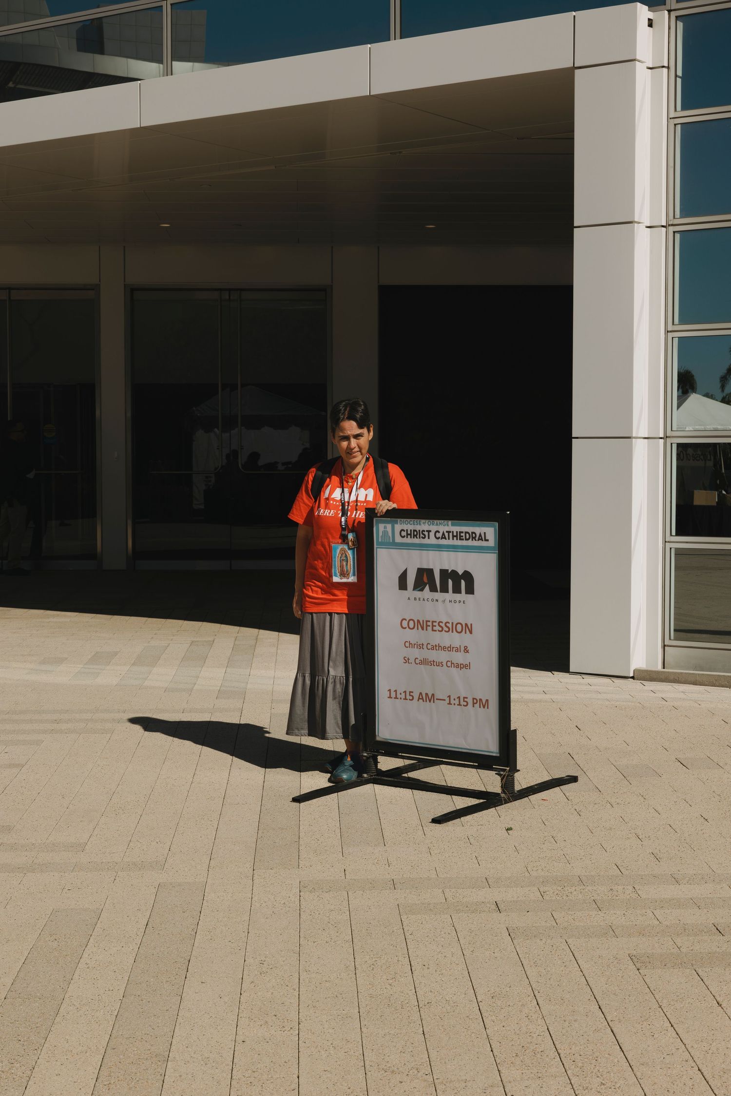 A volunteer stands next to a conference sign board outside a modern building entrance.