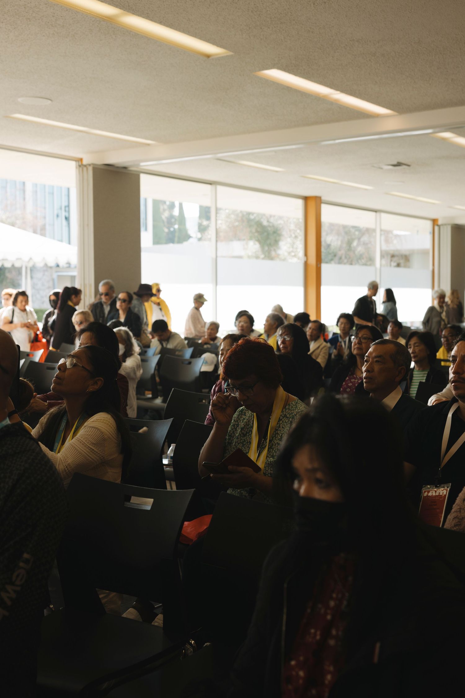Large crowd gathered in an indoor venue with natural lighting through windows.