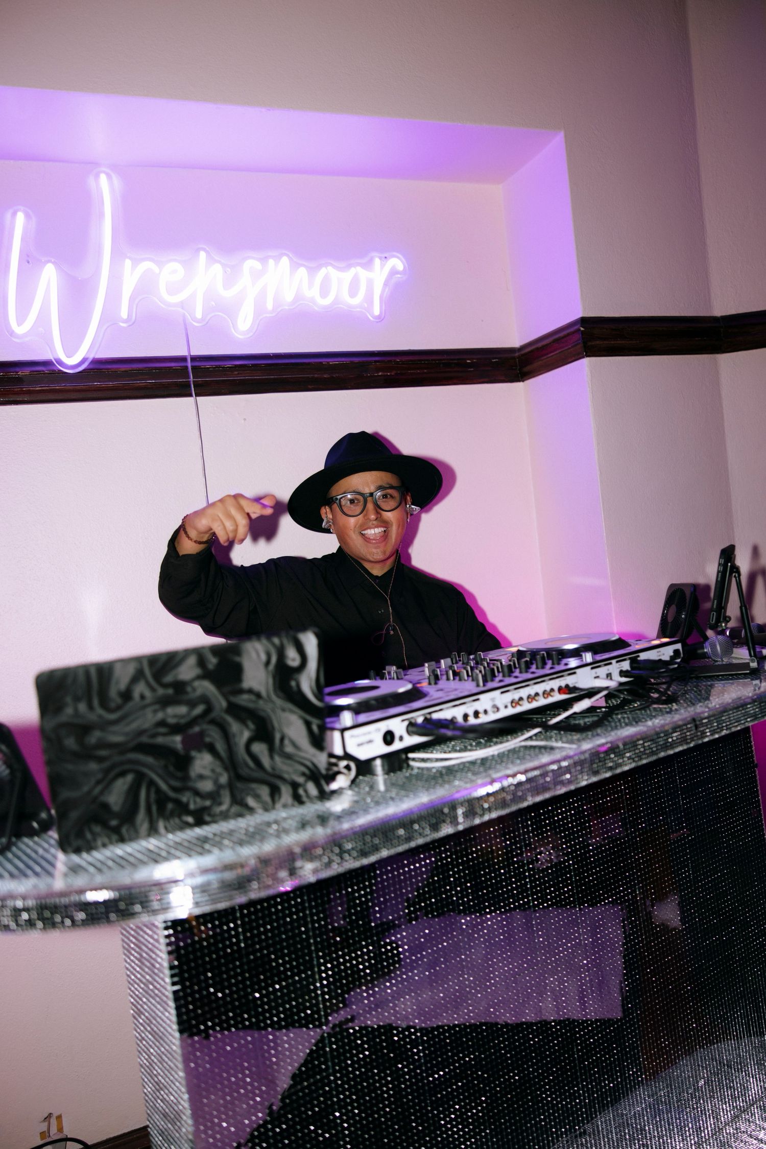 DJ performing under purple neon signage at a nightclub event.