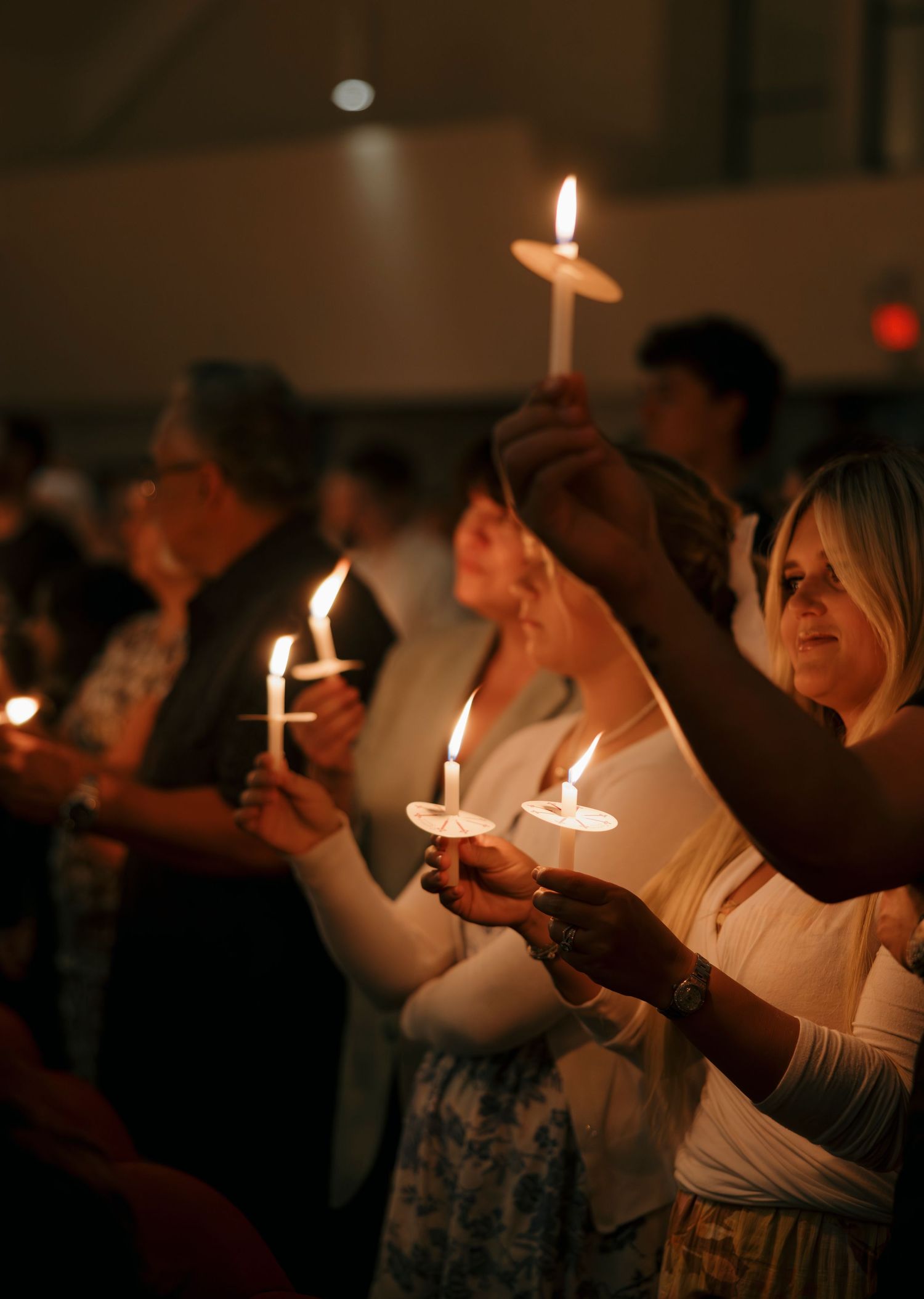 Congregation holds lit candles aloft during a candlelight church vigil service at night.