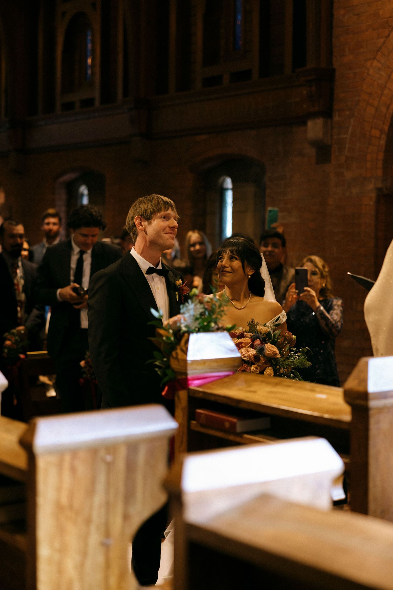 Wedding ceremony guests seated in wooden pews of a traditional brick church with arched ceilings.