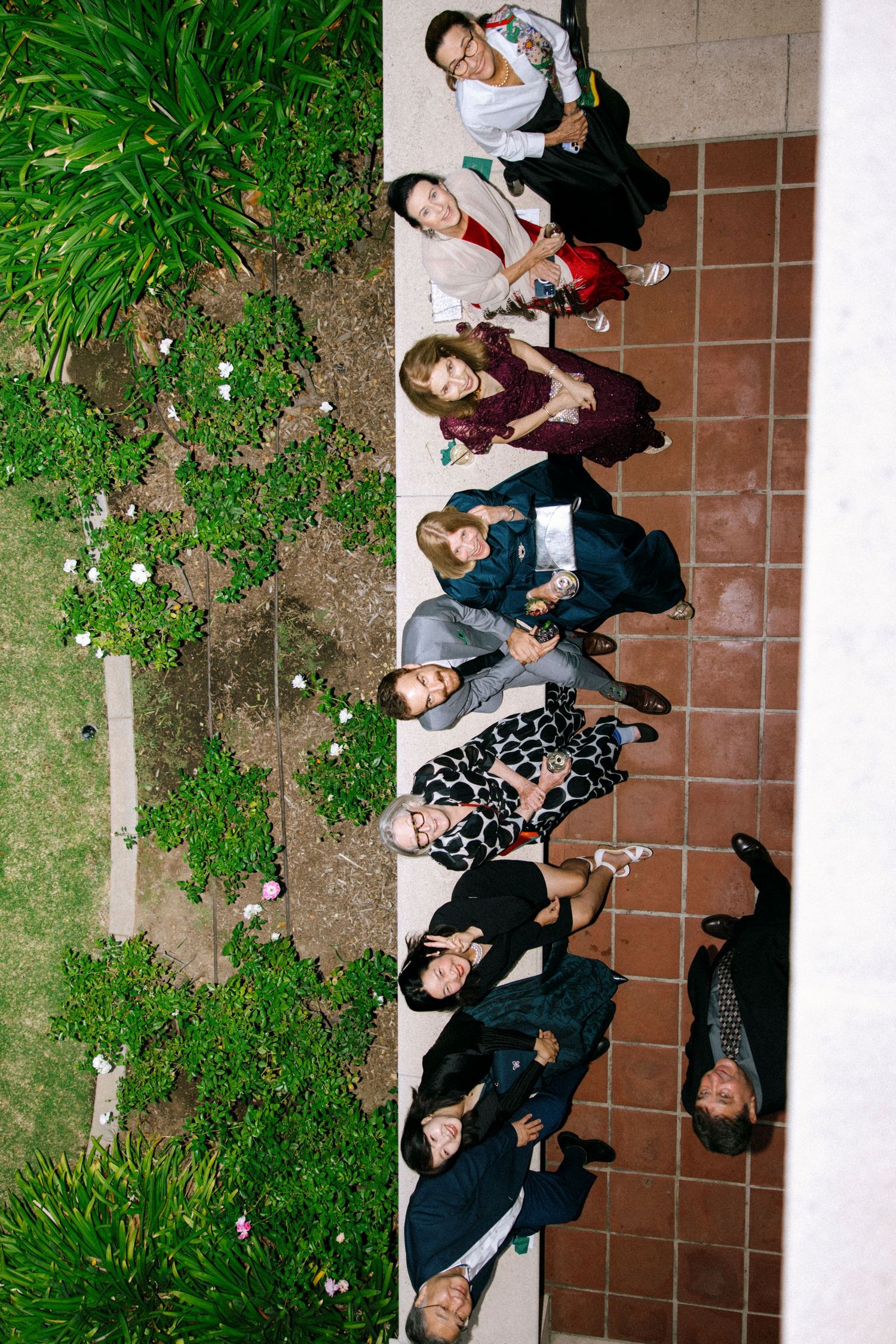 Creative overhead shot of wedding guests lying on grass and tiles forming a pattern.