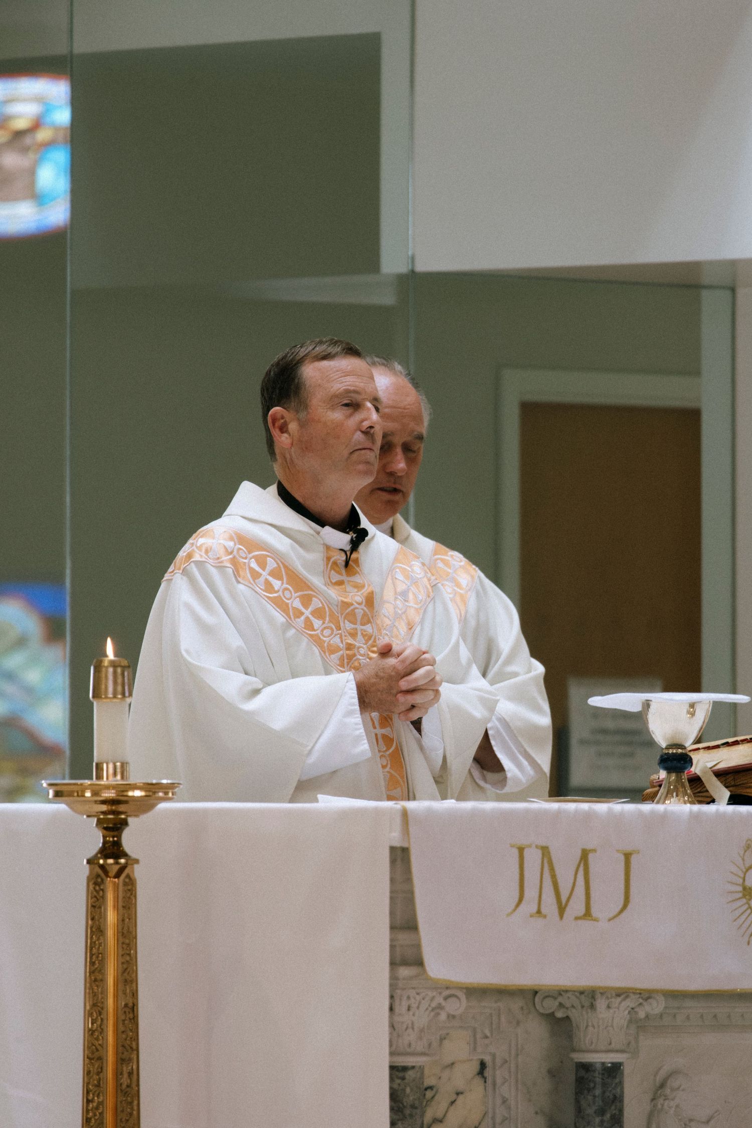 Priests in white robes performing religious ceremony at church altar.