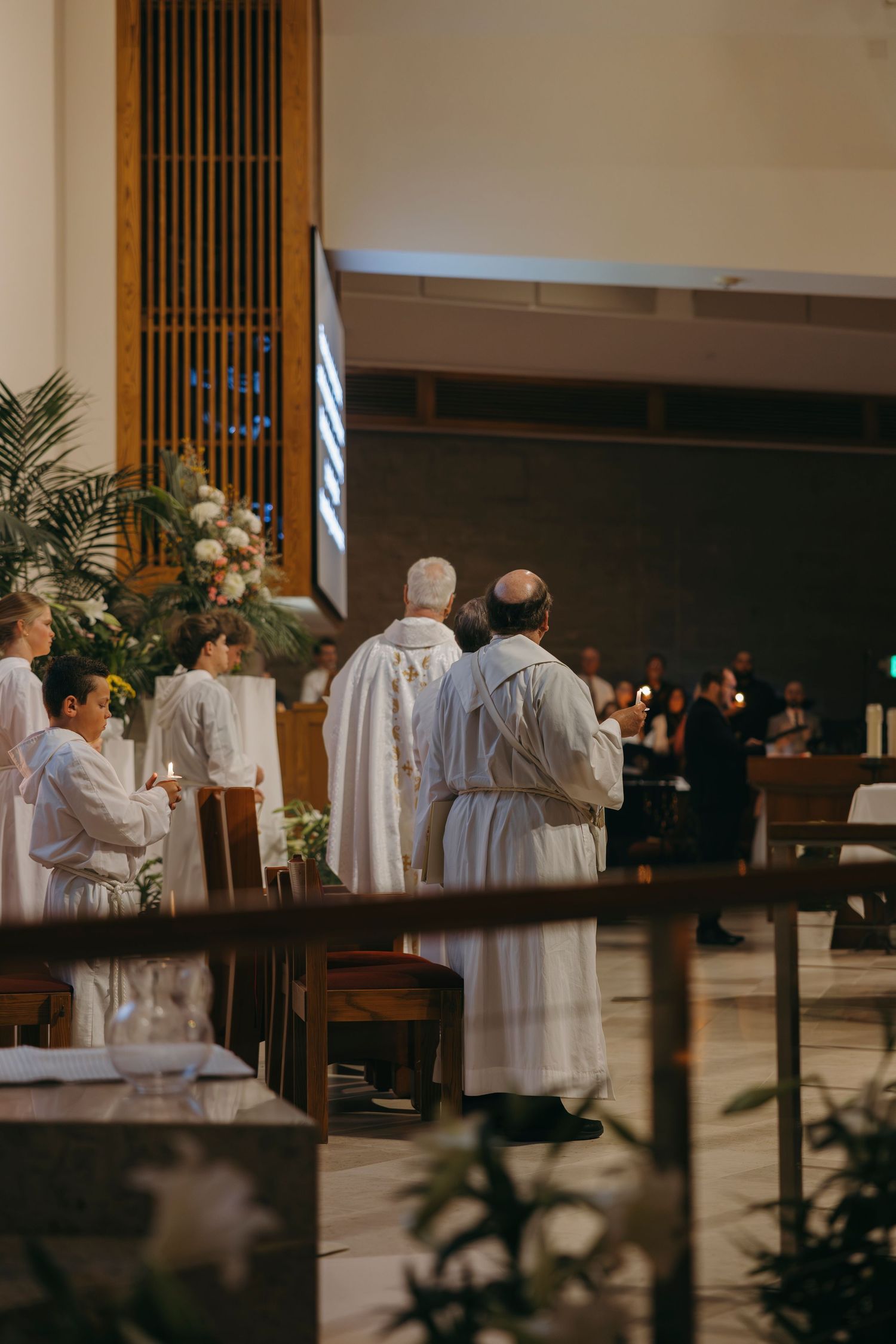 Catholic priests and altar servers in white vestments stand at altar during Easter Mass.