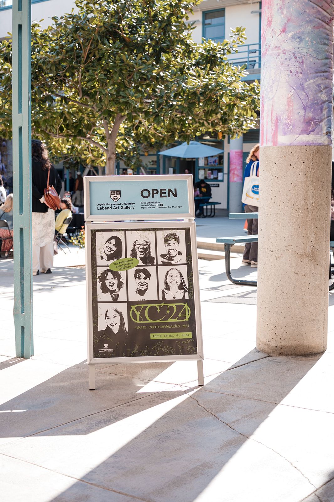 Outdoor sign displaying vintage-style portraits under tree shade.