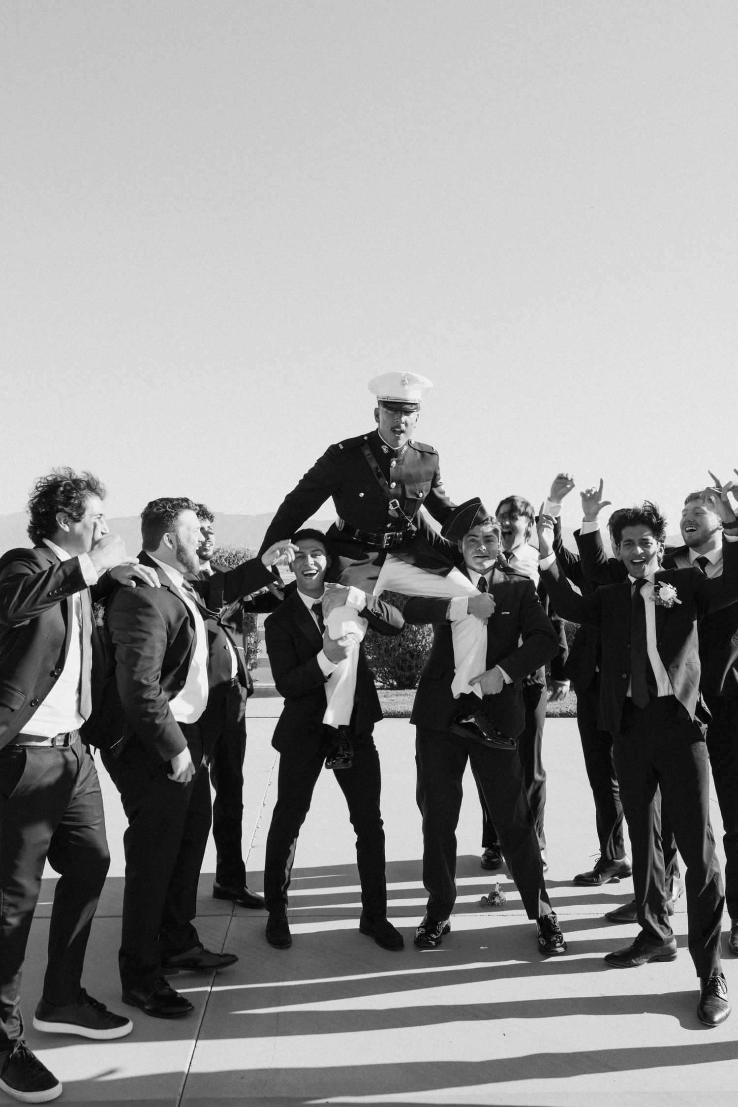 A line of people in formal attire leaning sideways in a synchronized pose against a white background.