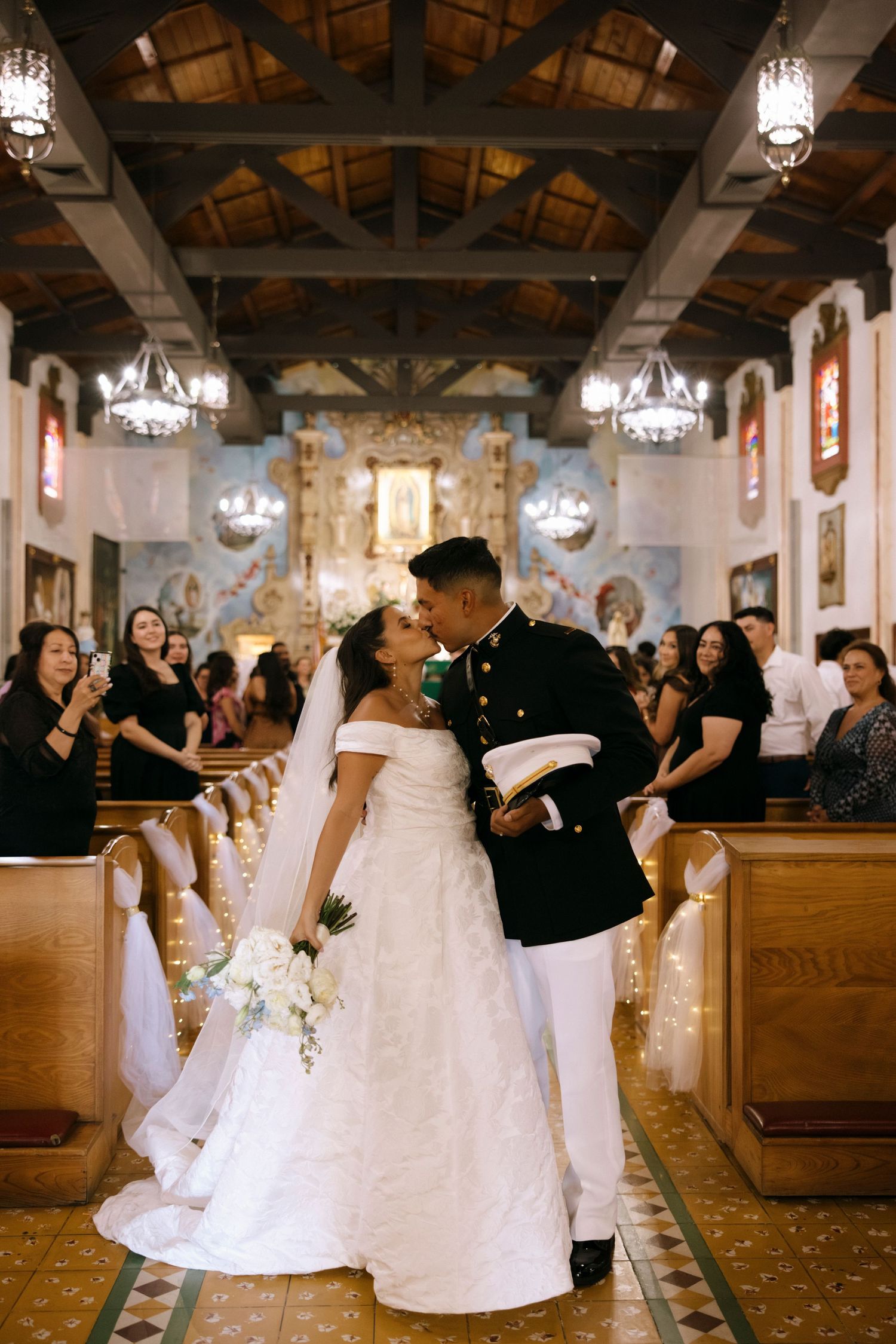 Couples dance and celebrate in a church reception hall with elegant chandeliers.