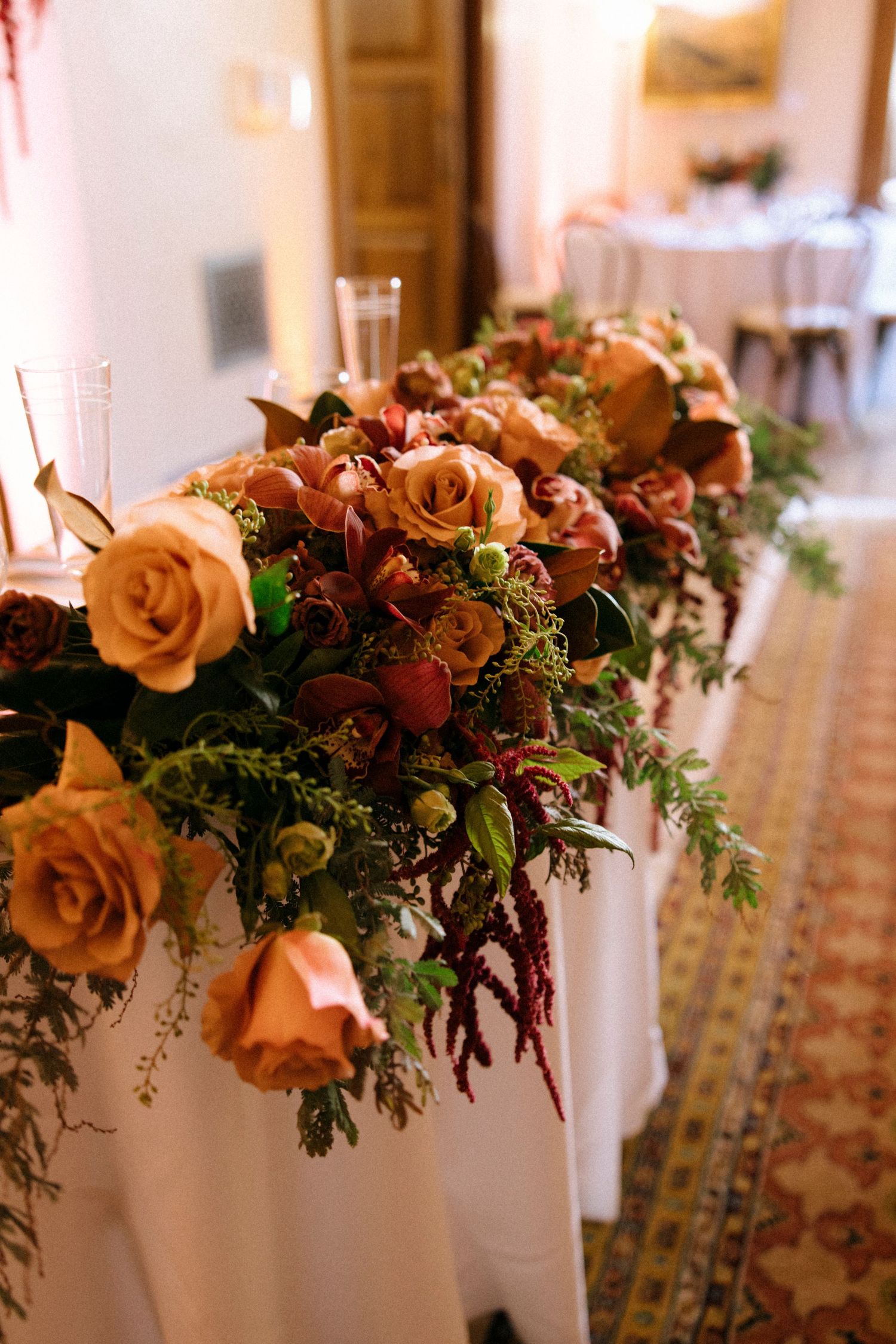 Lush floral centerpiece featuring peach roses and greenery on white tablecloth.