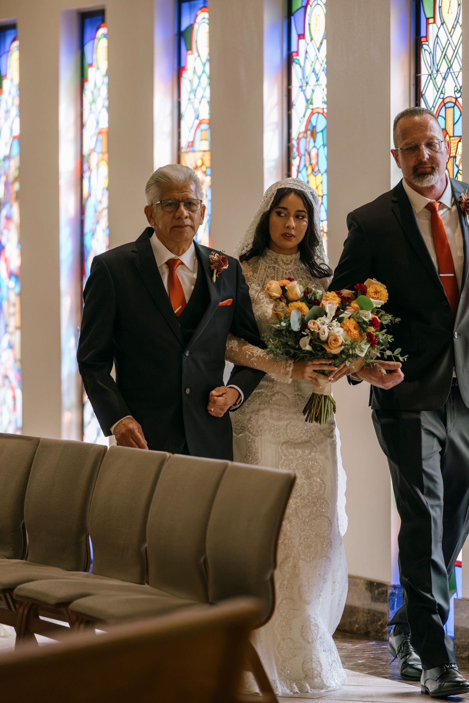 Wedding party standing beside church pews with colorful stained glass windows in the background.