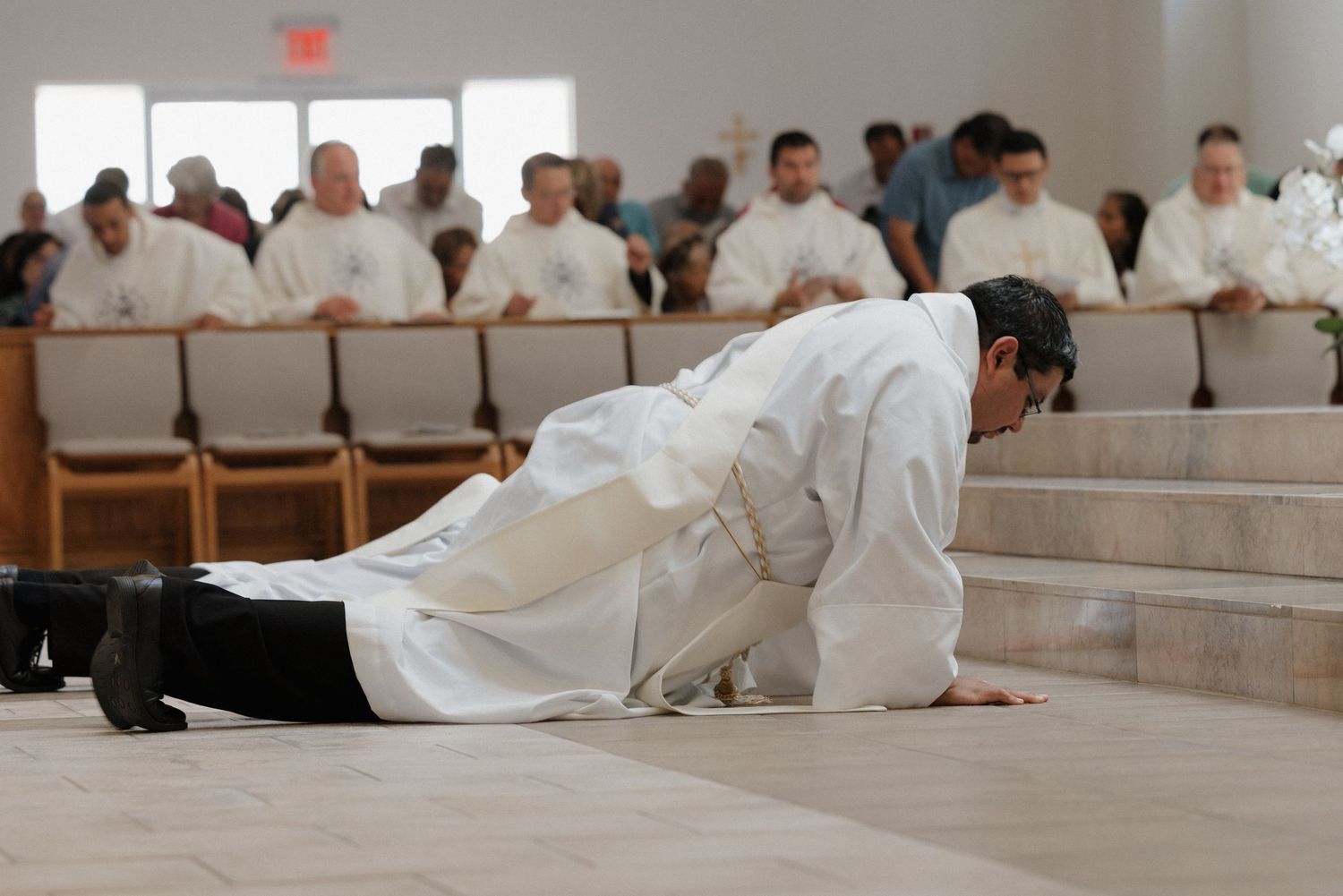 Clergy members in white robes prostrate themselves during an ordination ceremony.