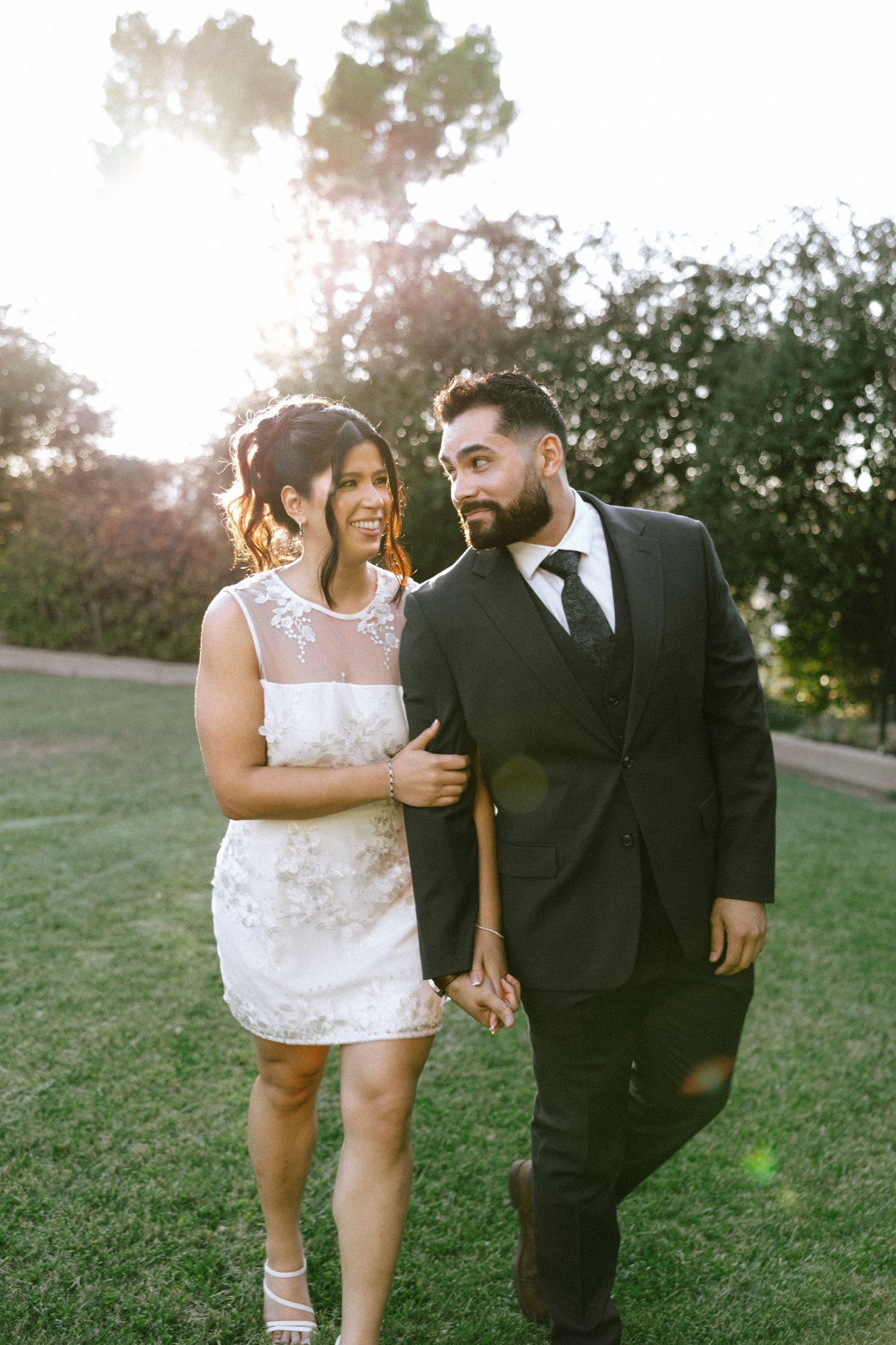 Newlyweds sharing joyful moment together on sunlit grassy hill.