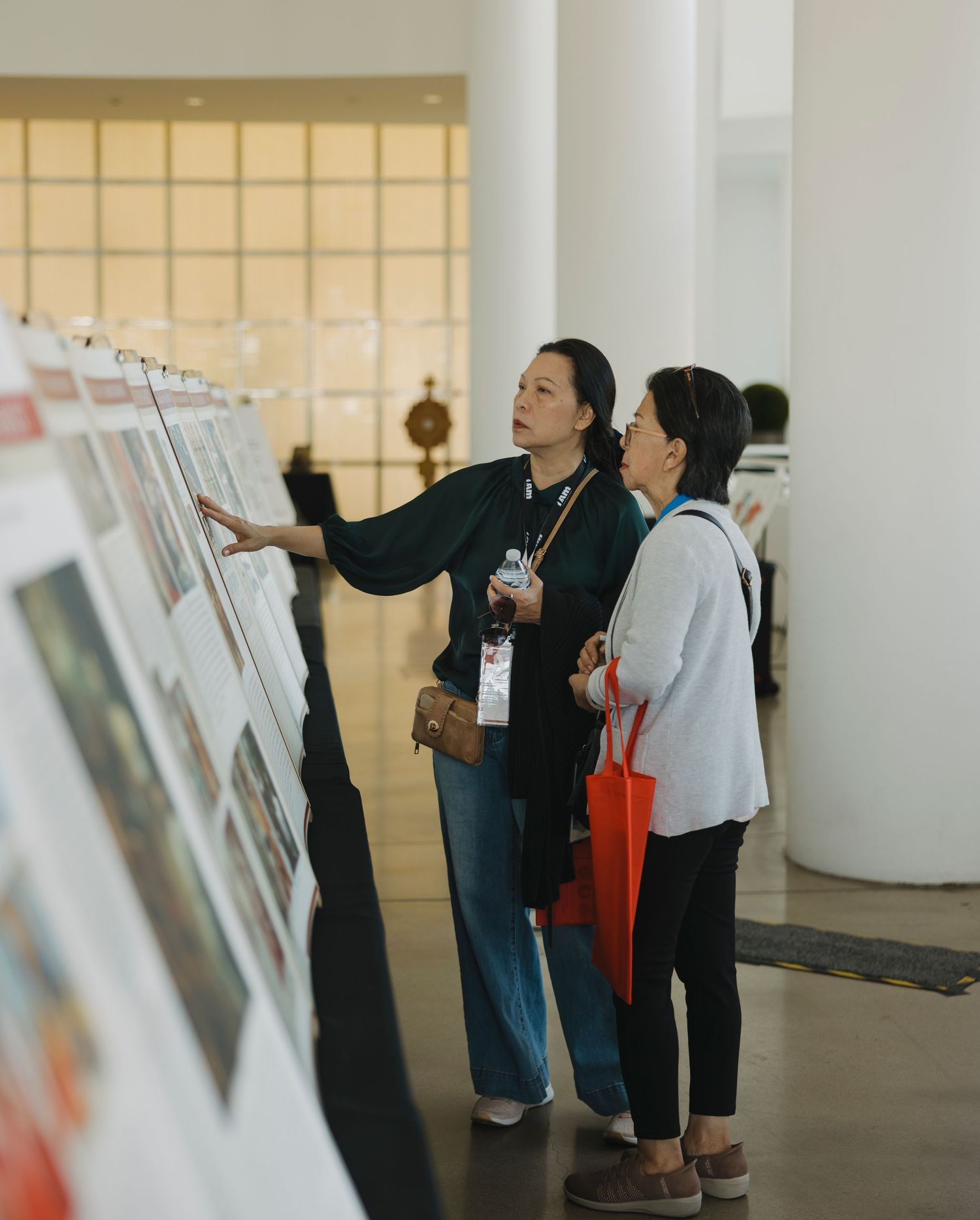 Visitors study artwork displays in a contemporary gallery space with white columns.
