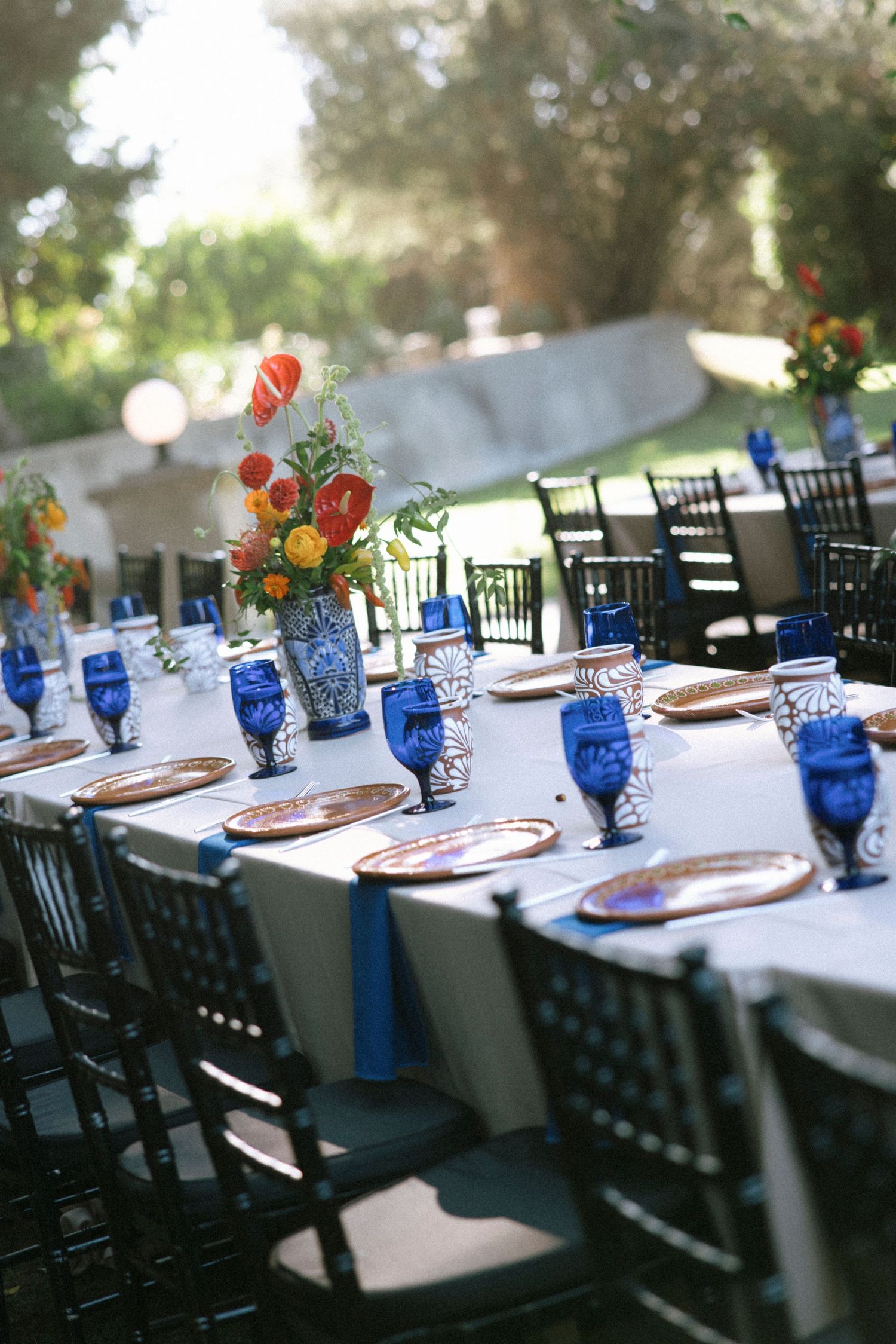 Wedding reception tables set with blue glassware, white linens, and colorful floral centerpieces.