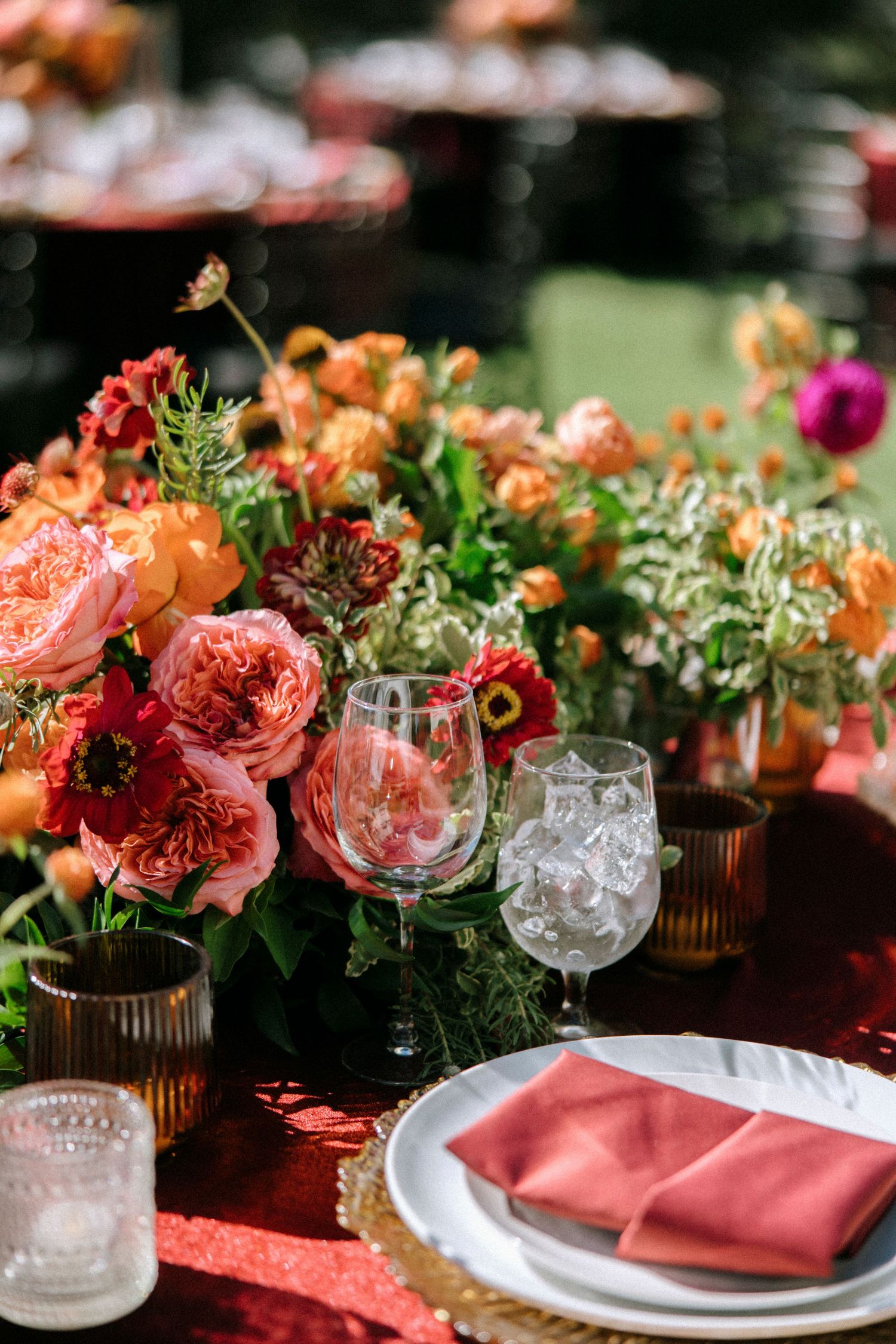 Close-up of coral and pink floral arrangements with crystal glassware on a formal dining table.