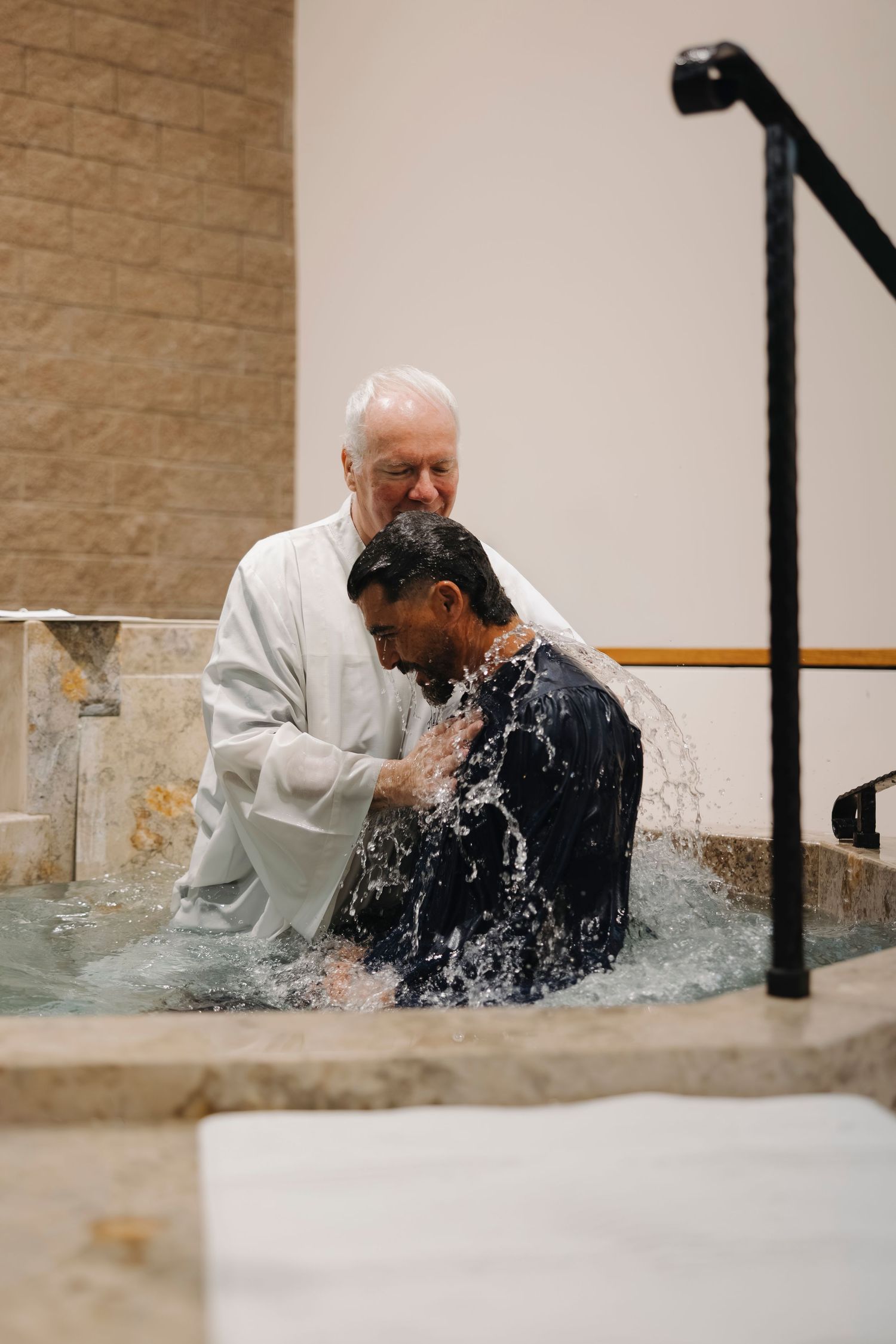 Priest performing a full immersion baptism in a baptismal pool.