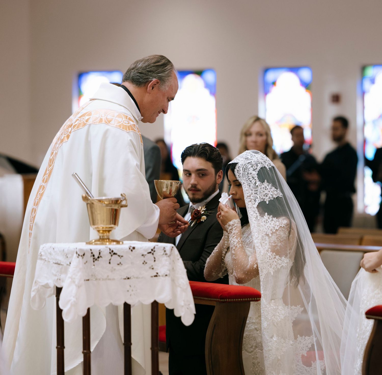 Religious wedding ceremony in progress with bride in lace veil at church altar.