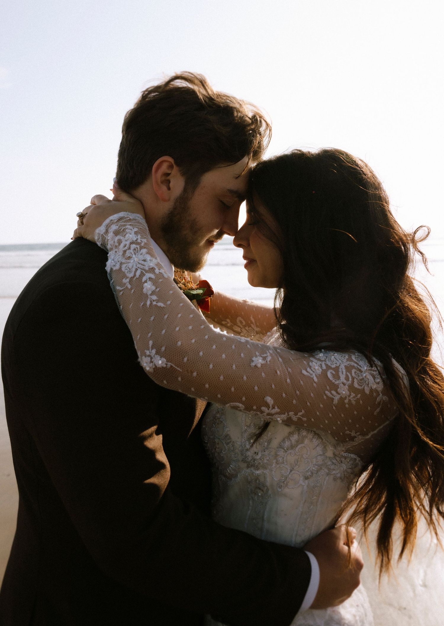 Silhouetted couple in wedding attire sharing an intimate moment against bright sky.