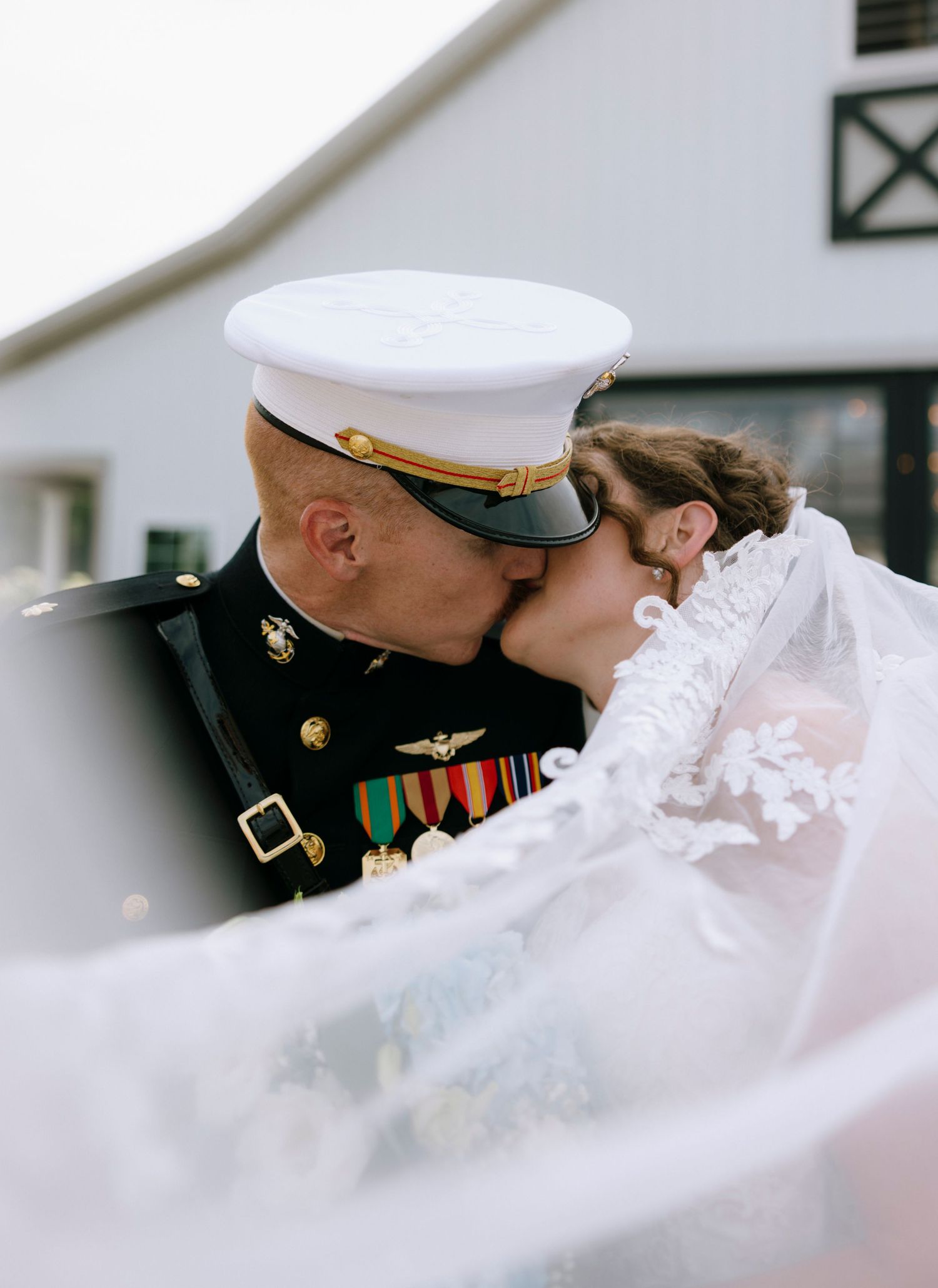A Marine in dress uniform shares a romantic kiss with his bride in a flowing lace veil on their wedding day.