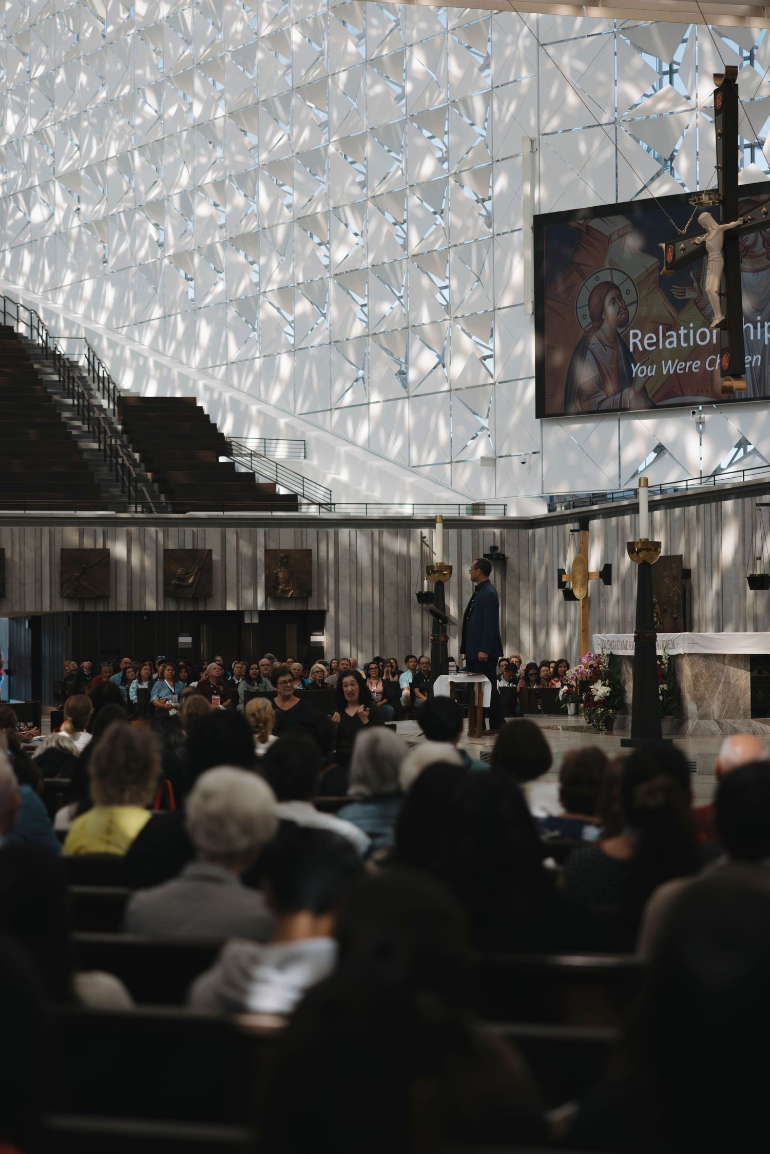 A large congregation gathered in a modern church with distinctive geometric ceiling patterns.