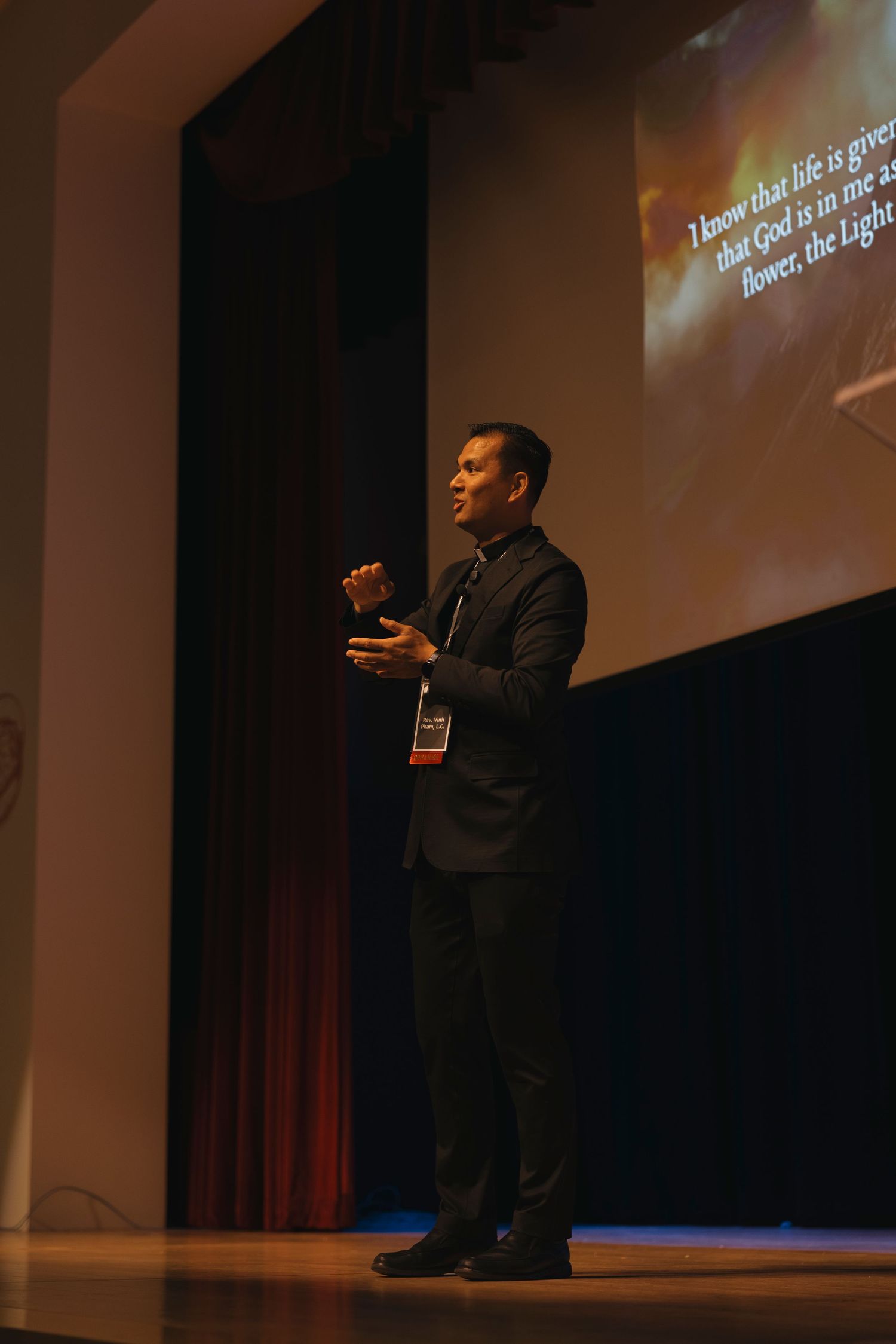 A speaker delivers a presentation on stage with dramatic lighting and projected visuals.