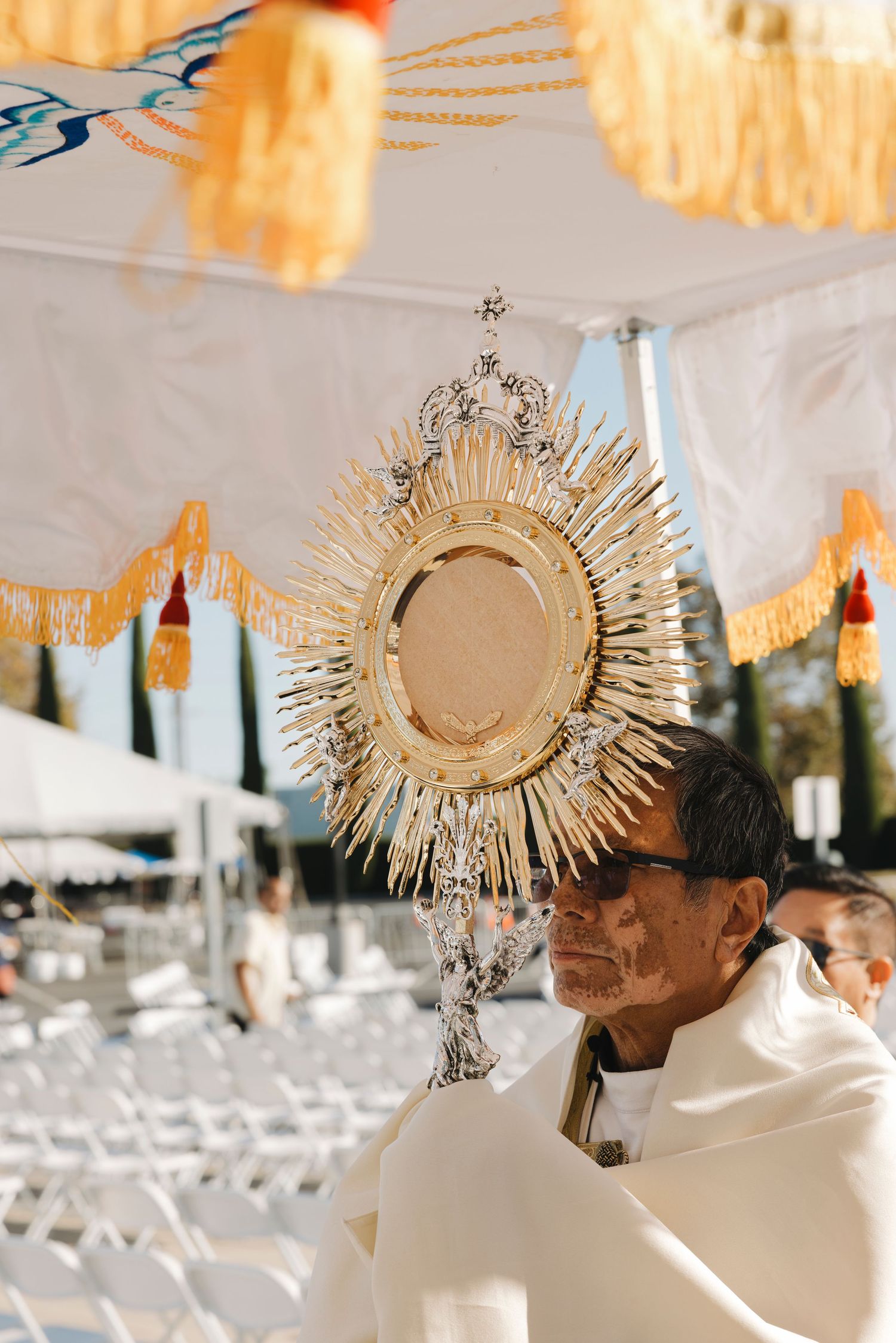 Golden monstrance displayed under decorated white canopy during Catholic ceremony.