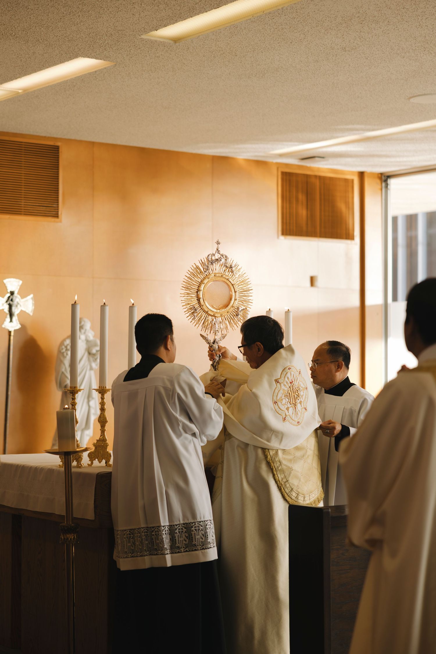 Clergy members in white robes gather near religious artifacts in a warmly lit chapel setting.