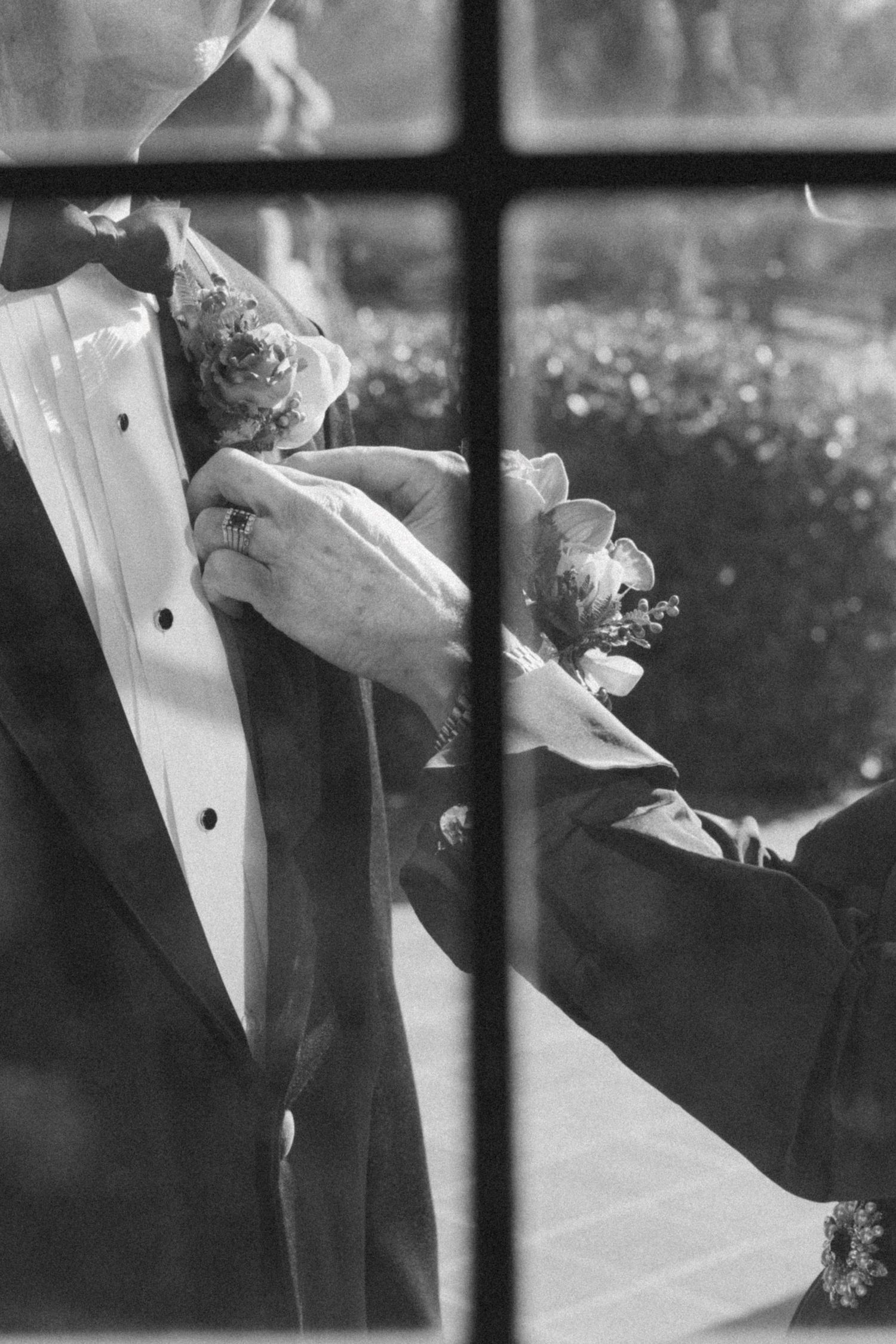 Black and white detail shot of formal attire and bouquet through window panes.