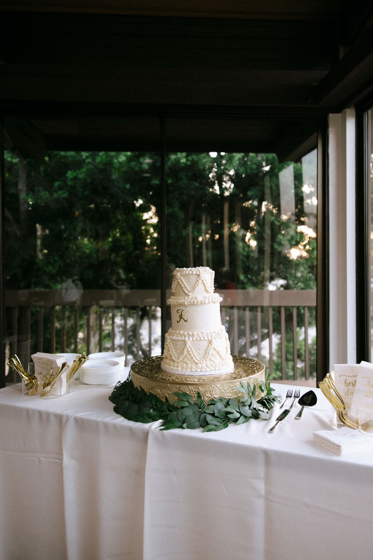 Three elegant white wedding cakes displayed on a long table with white linens and natural lighting.