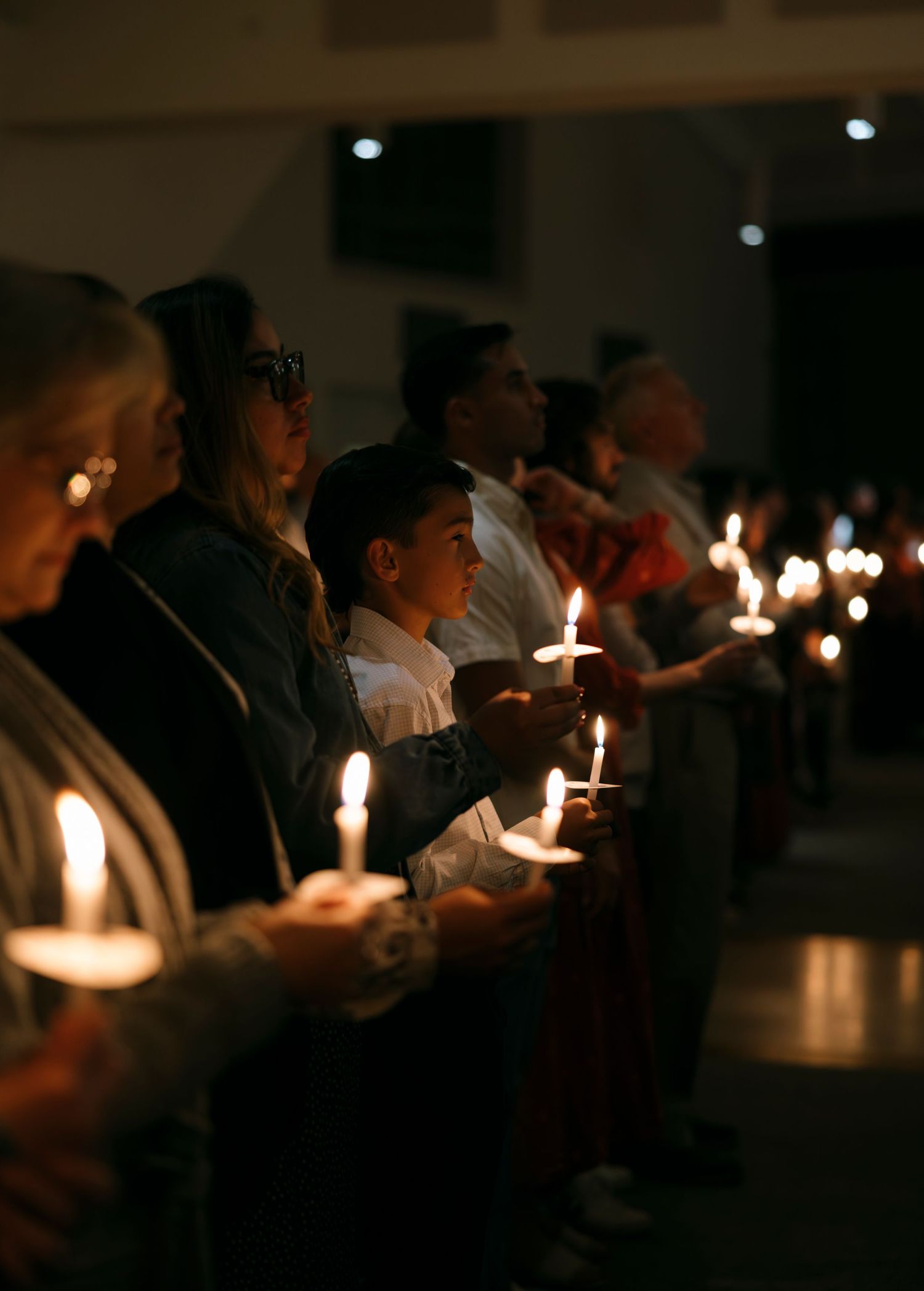 Parishioners including young boy holding glowing candles during Easter Vigil Mass ceremony.