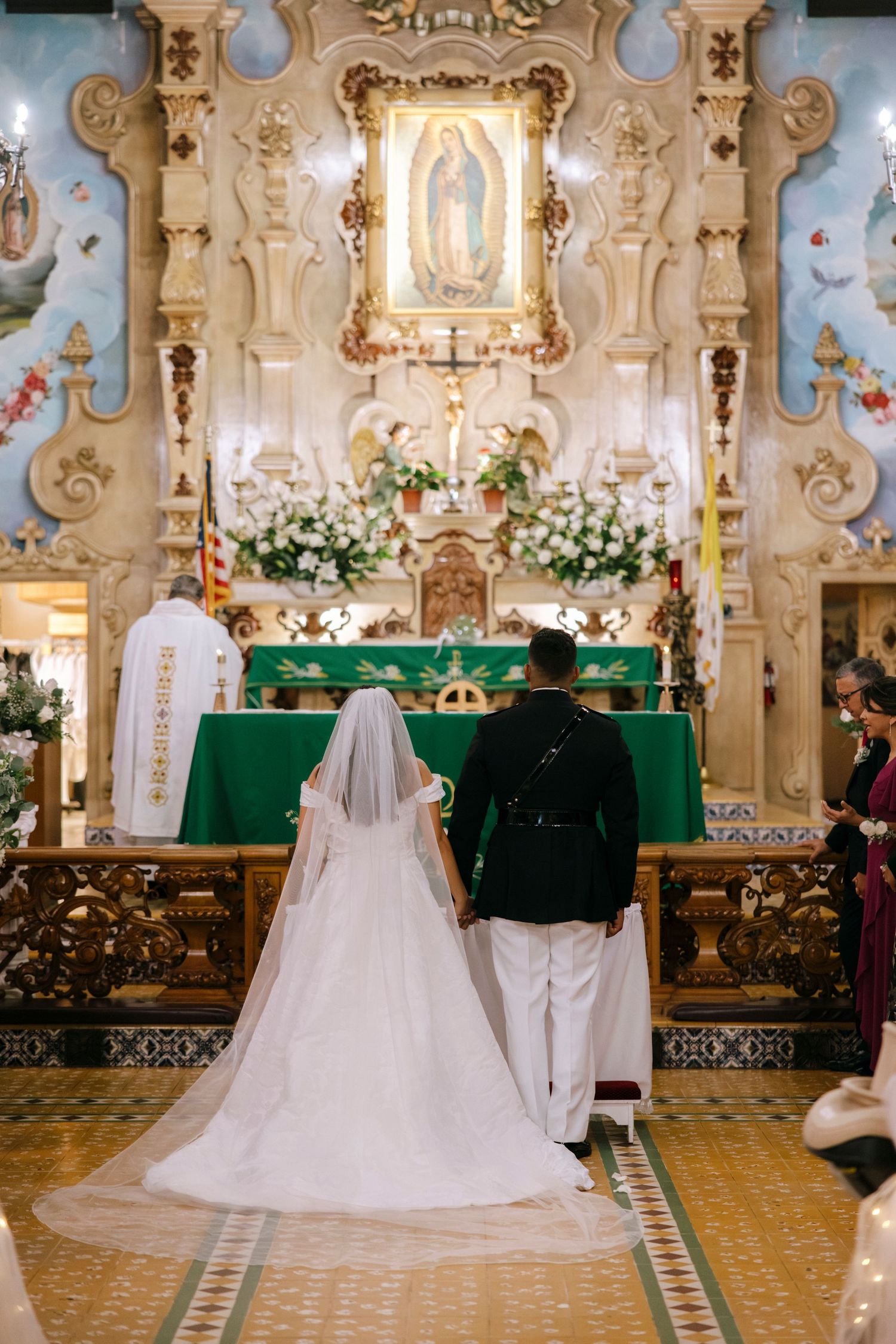 An ornate church interior decorated with white flowers and green altar cloths for a wedding ceremony.