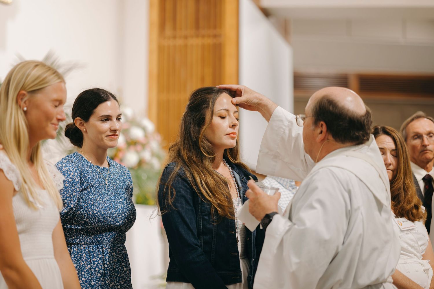 Catholic priest anointing a young woman with chrism oil during a confirmation sacrament ceremony.