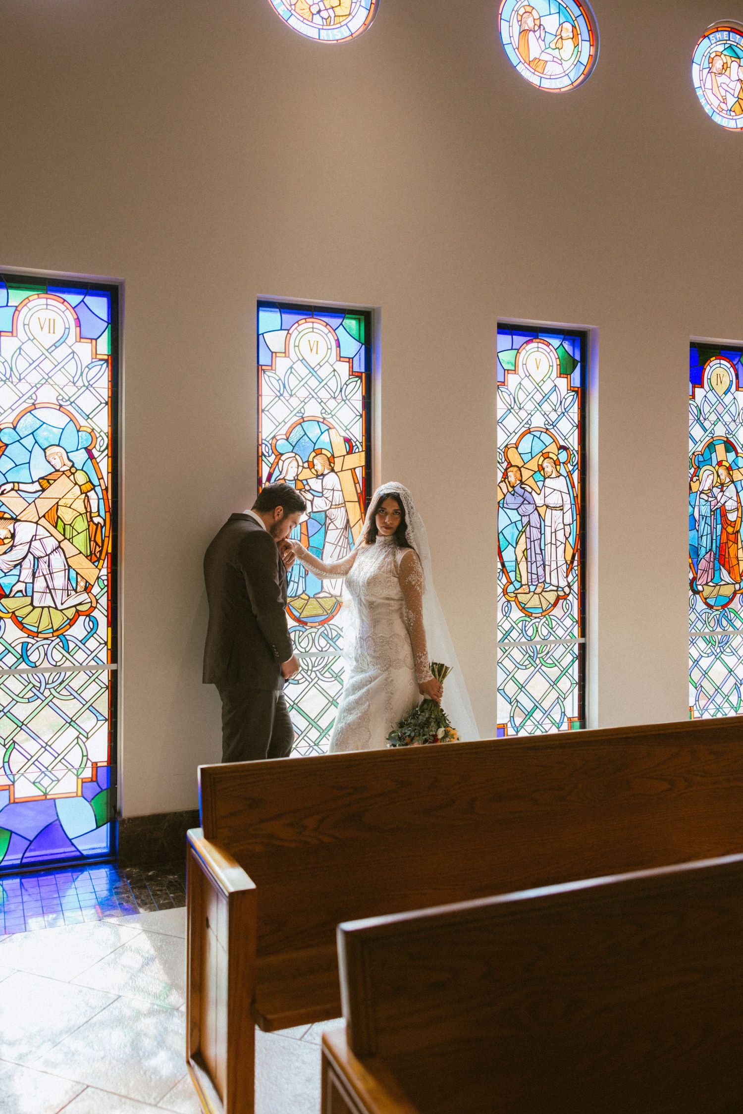 A couple shares a moment beneath colorful stained glass windows in a church.