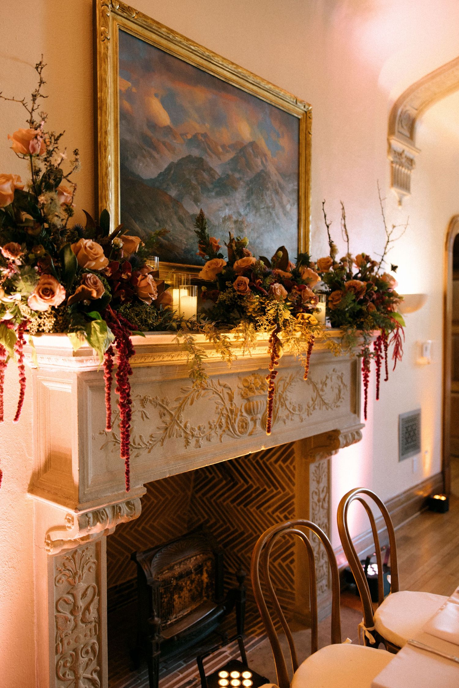 Ornate fireplace mantel decorated with floral arrangements and framed by gold-trimmed artwork.
