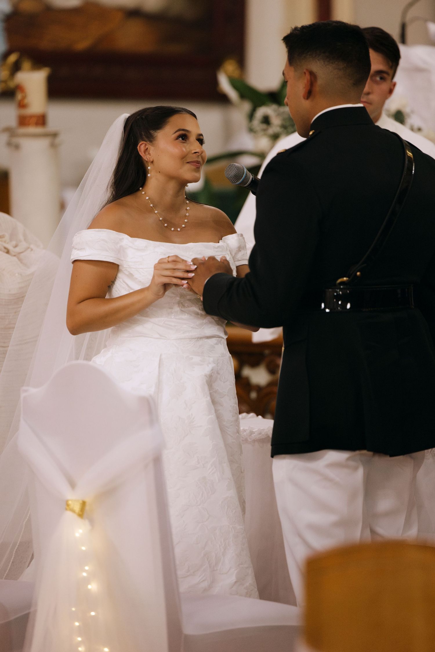 A bride in white gown exchanges rings with groom in military uniform during church ceremony.