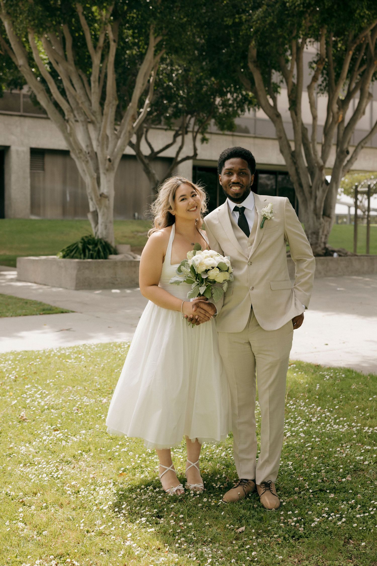 Newlyweds share a joyful moment outdoors among trees on their wedding day.