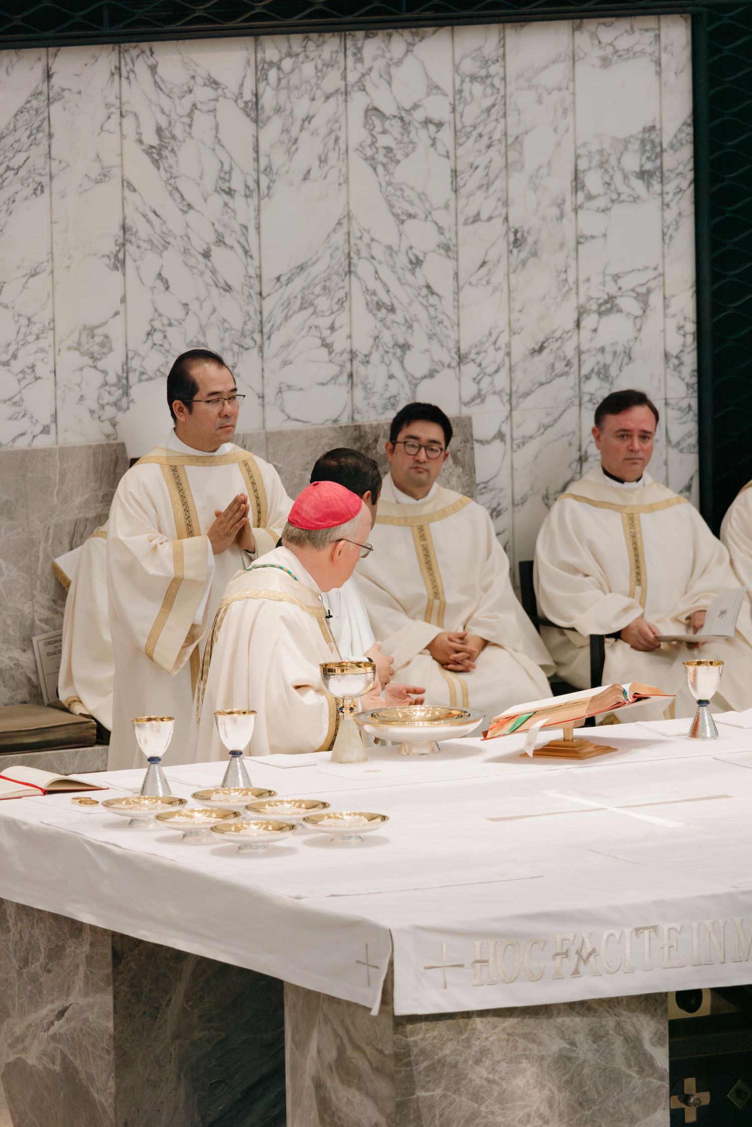 Clergy members in white vestments seated at a long table during a religious ceremony.