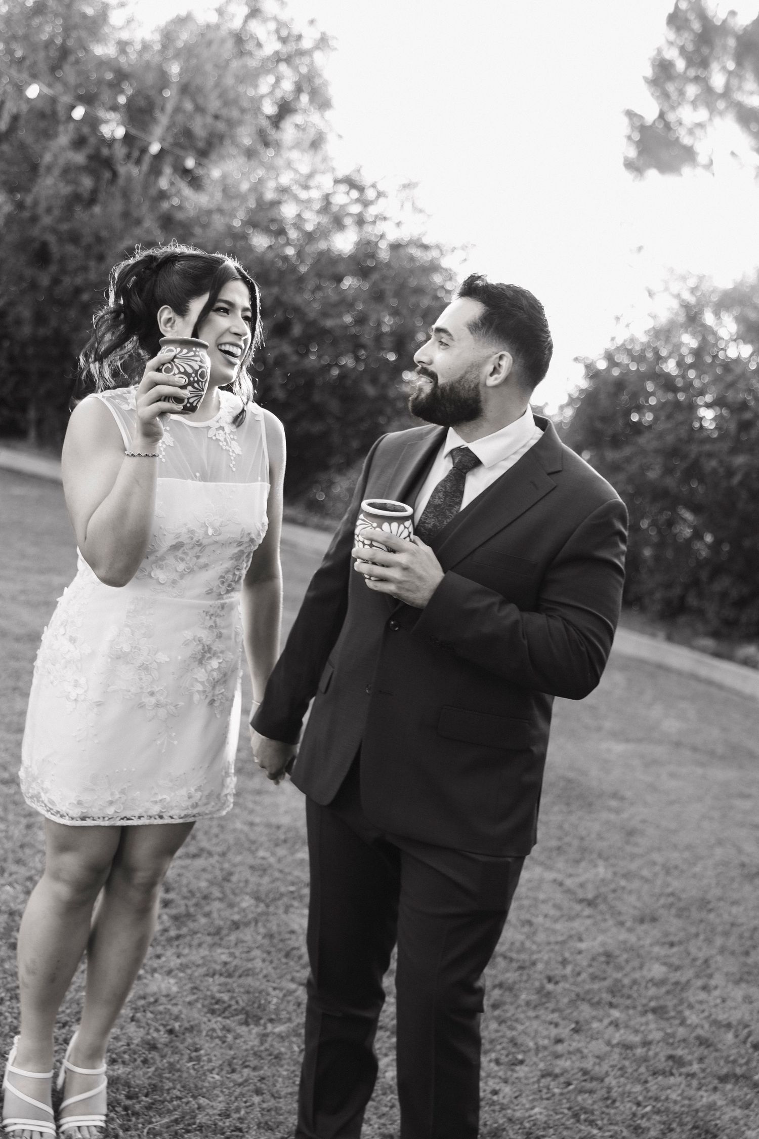 Couple enjoying drinks and laughter during outdoor wedding photo session.