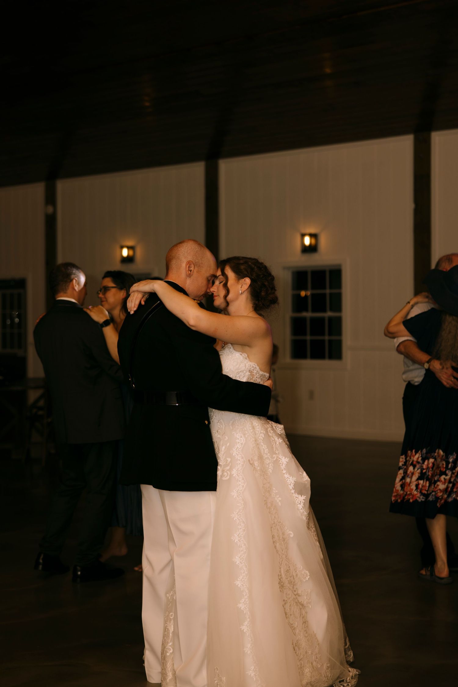 Bride and groom share their first dance at a romantic indoor wedding reception in a rustic white barn venue.