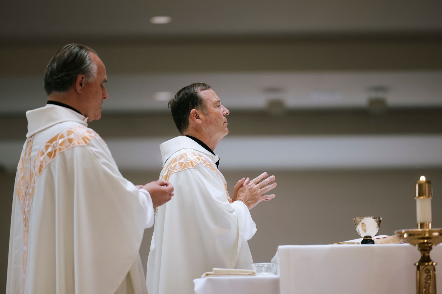 Clergy in white robes performing religious ceremony at church altar.