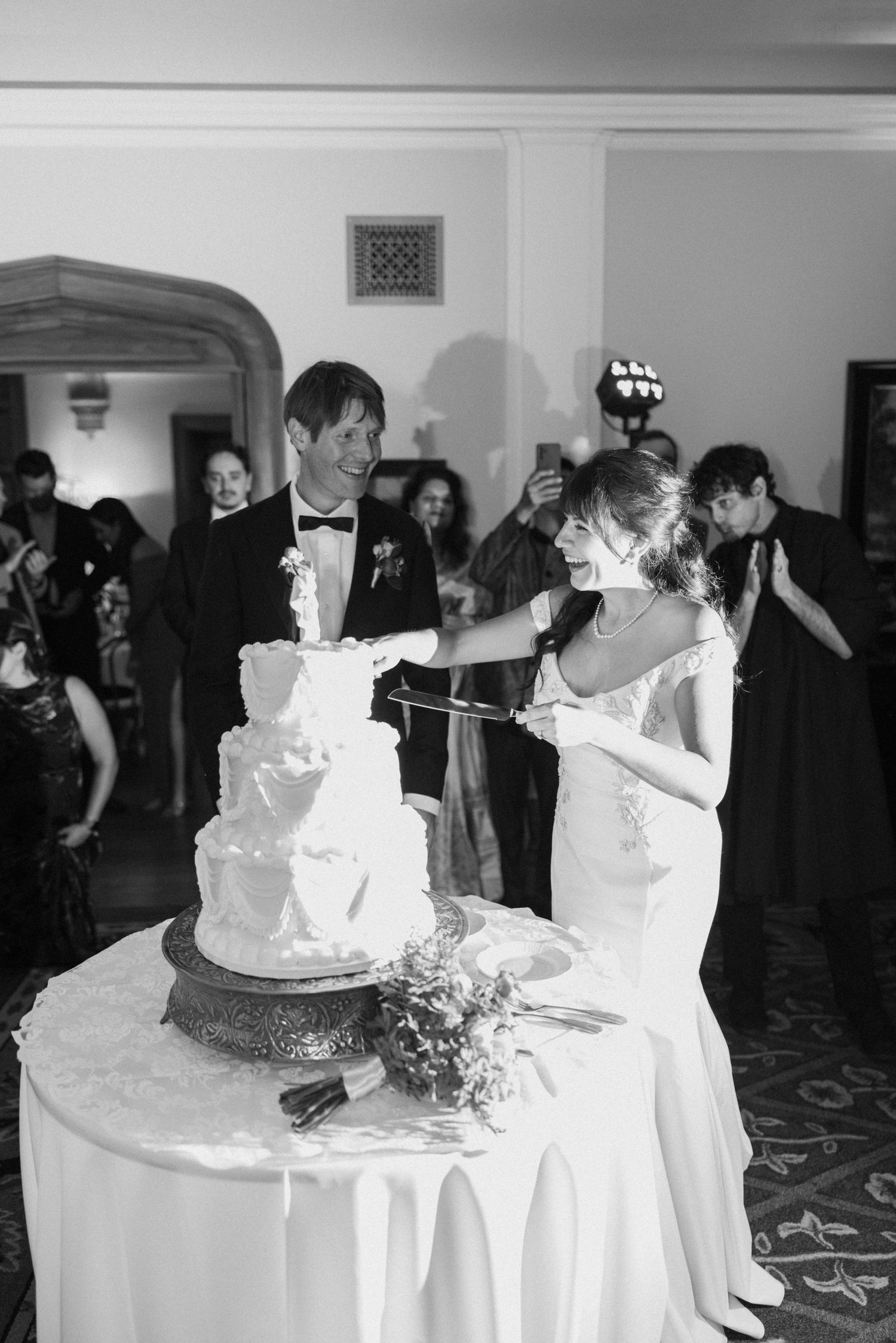 Wedding cake cutting ceremony with multiple tiers of white cake on display.