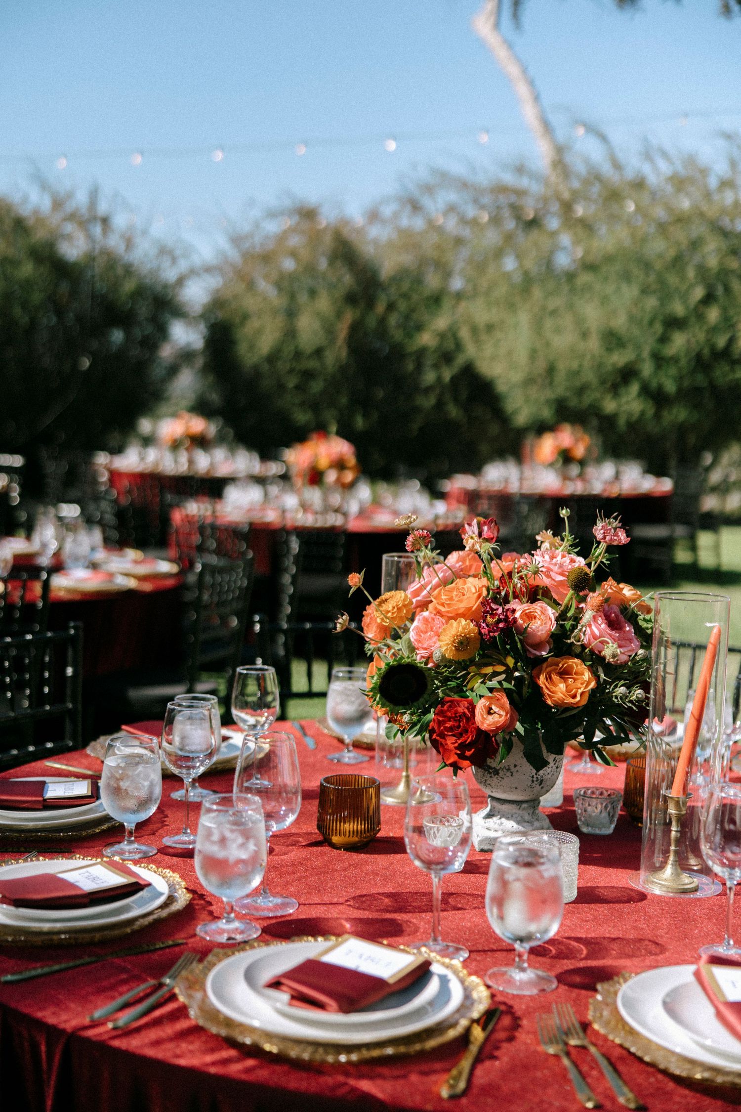 Elegant table settings with coral linens and floral centerpieces arranged for an outdoor wedding reception.