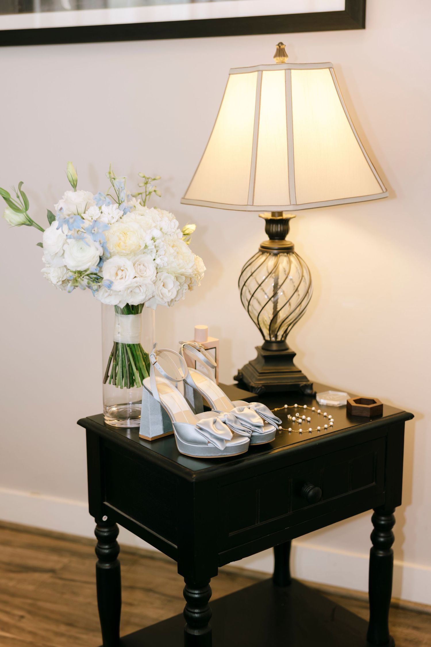 Elegant side table with lamp and white floral arrangement in wedding preparation room.