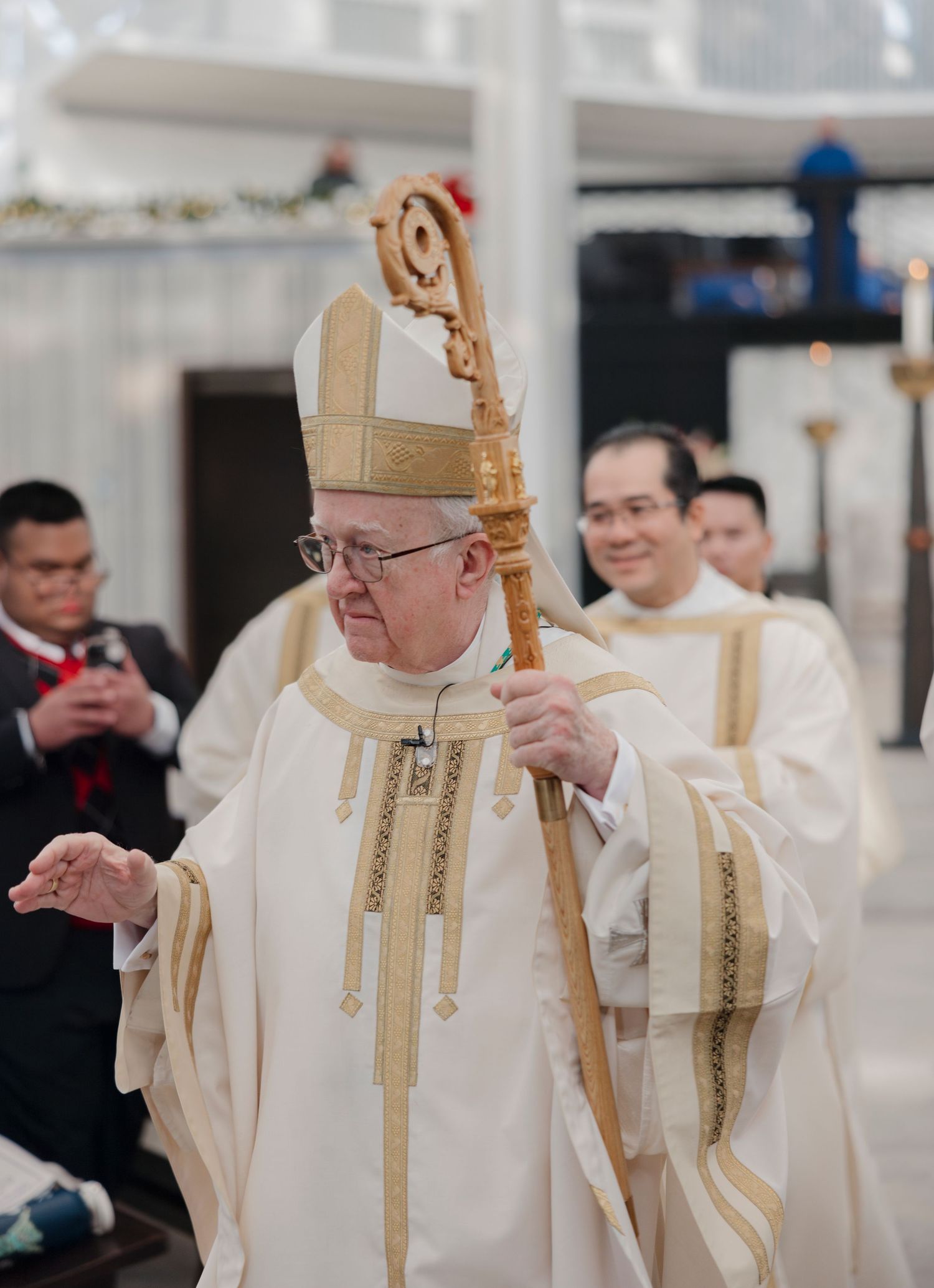 Catholic clergy in white and gold vestments performing religious ceremony at altar.