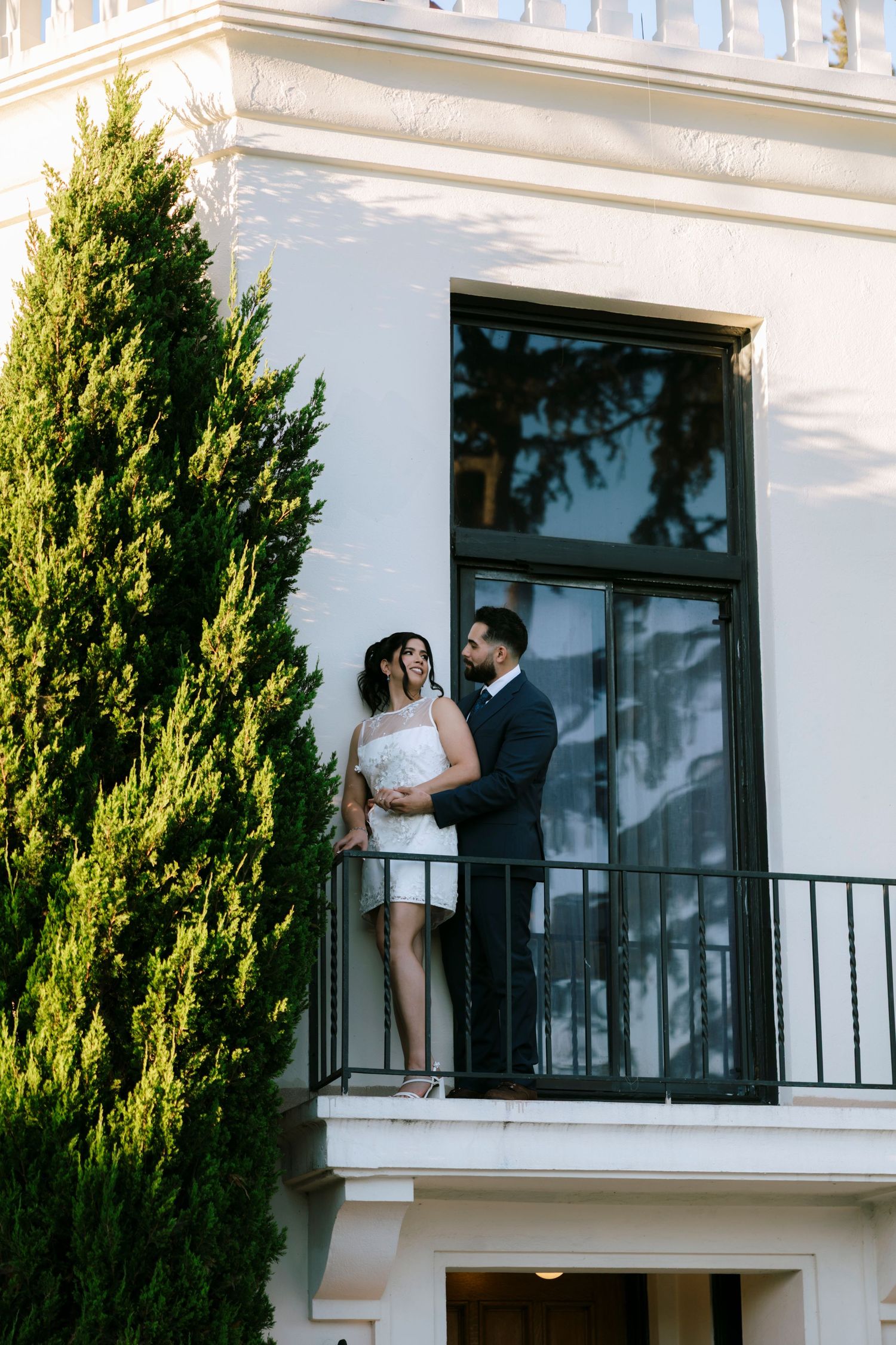 A couple shares a romantic moment on a balcony of a white building.
