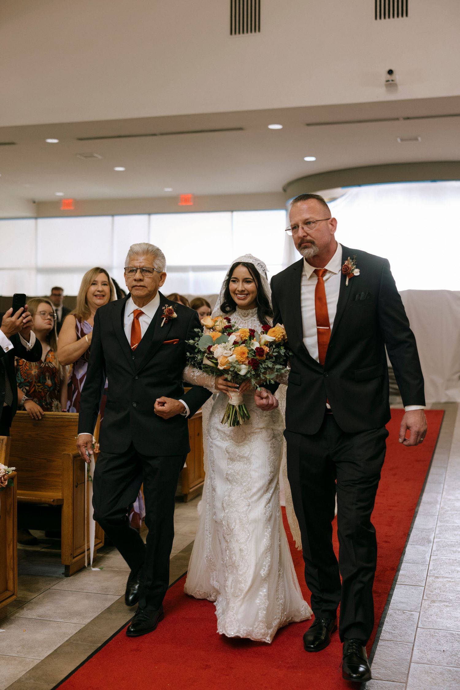 Wedding party walking down church aisle with floral bouquets and formal attire.