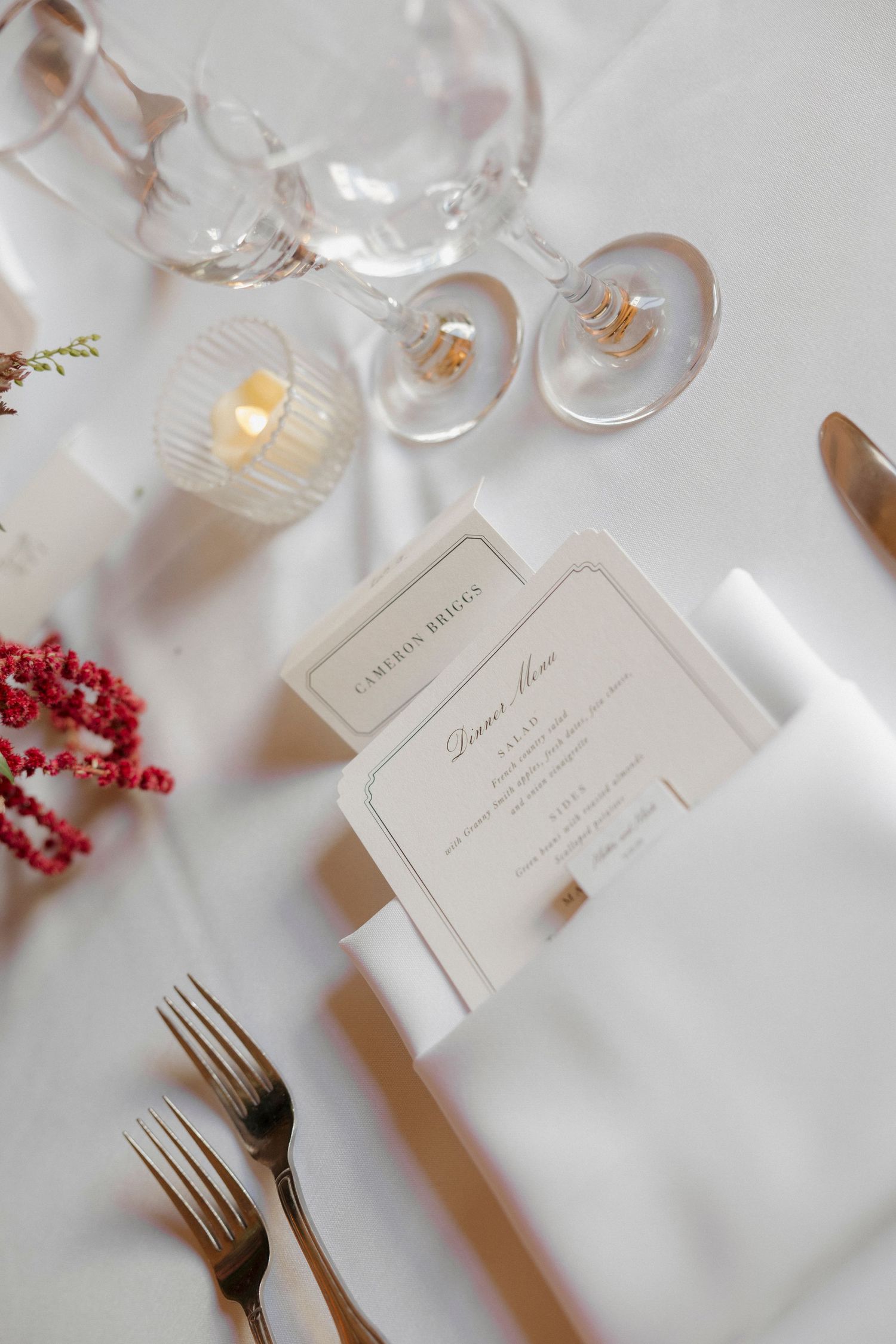 Elegant place settings with wine glasses and menu cards on a white tablecloth at an upscale event.