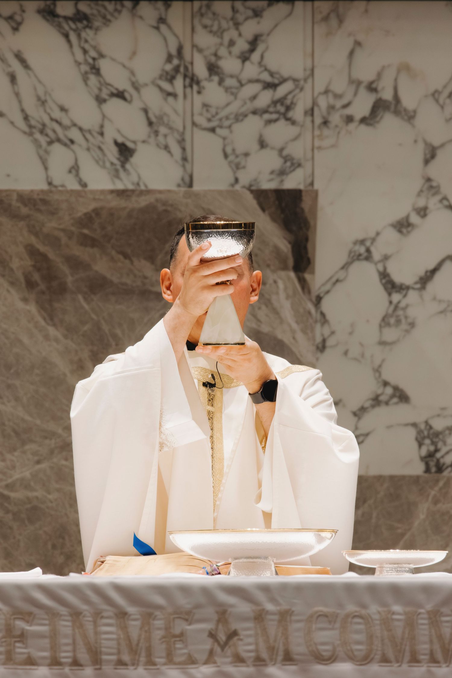 Priest elevating chalice during Catholic mass at marble altar.